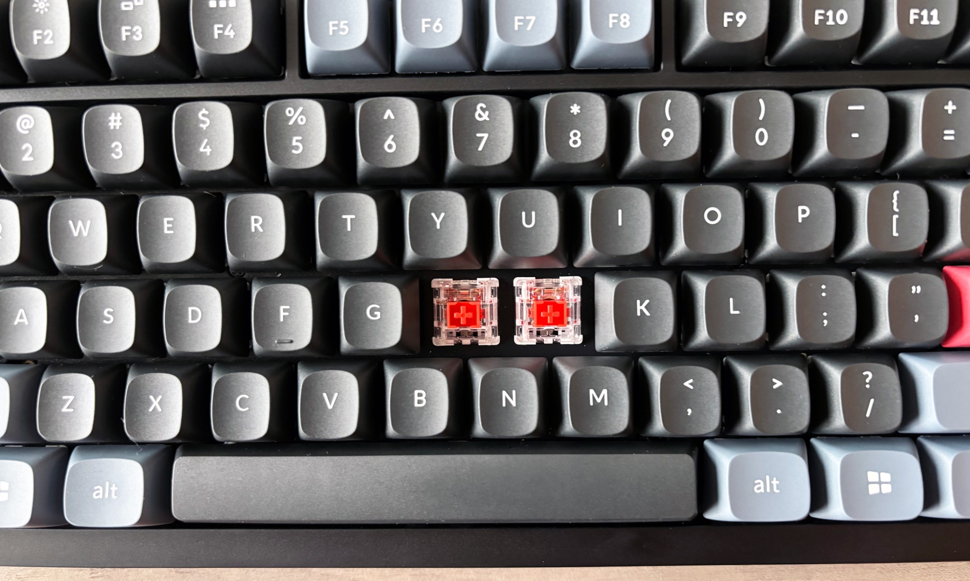 A close-up of a gaming keyboard with two keycaps removed, displaying the switches underneath.