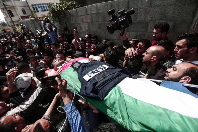 Murtaja’s body, covered in a Palestinian flag and a “Press” vest, is carred through a crowd.