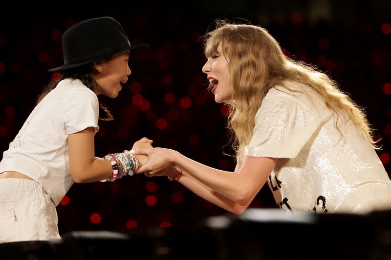 Taylor Swift happily holding the hands of a young fan.