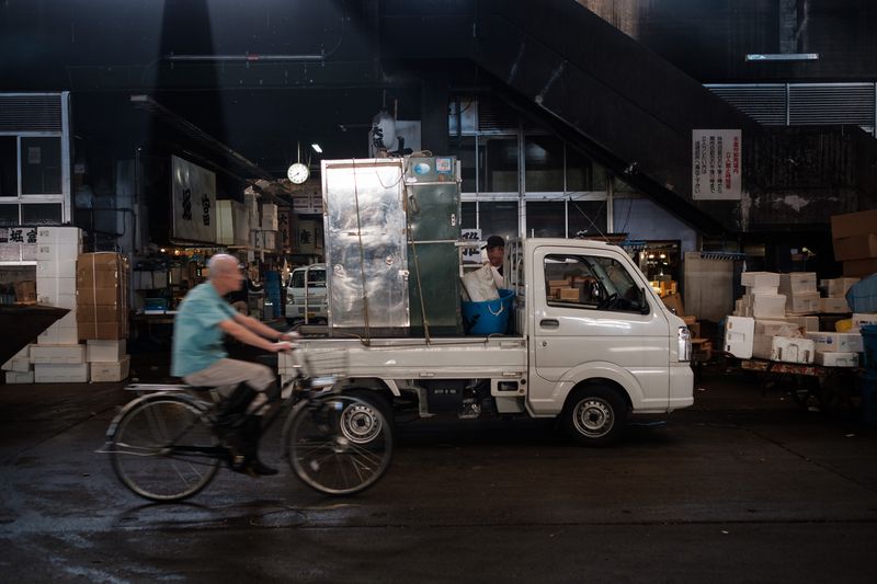 A cyclist passes a small pickup truck not much taller than the height of a human making a nighttime delivery.