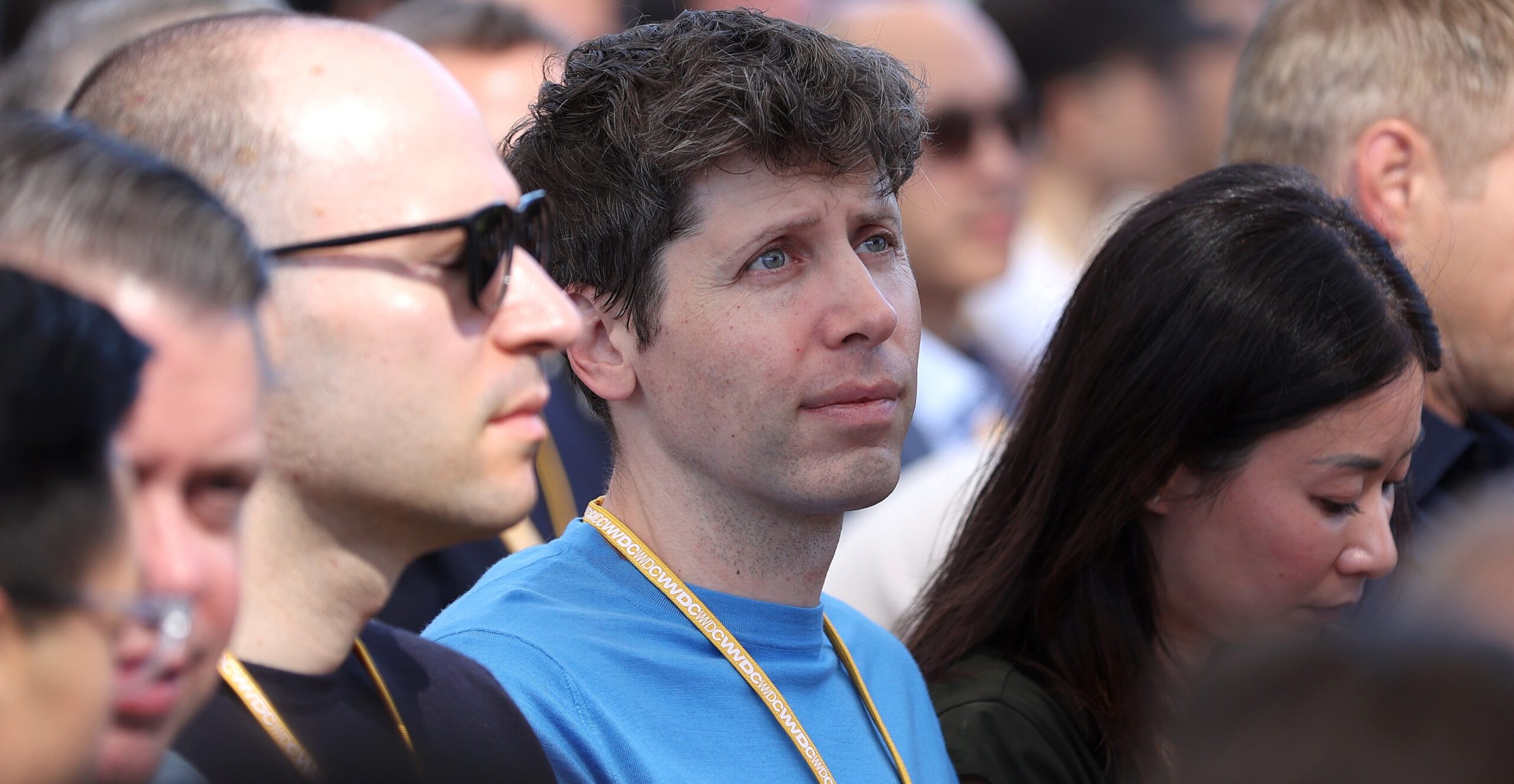 OpenAI CEO Sam Altman sits in a crowd at WWDC.