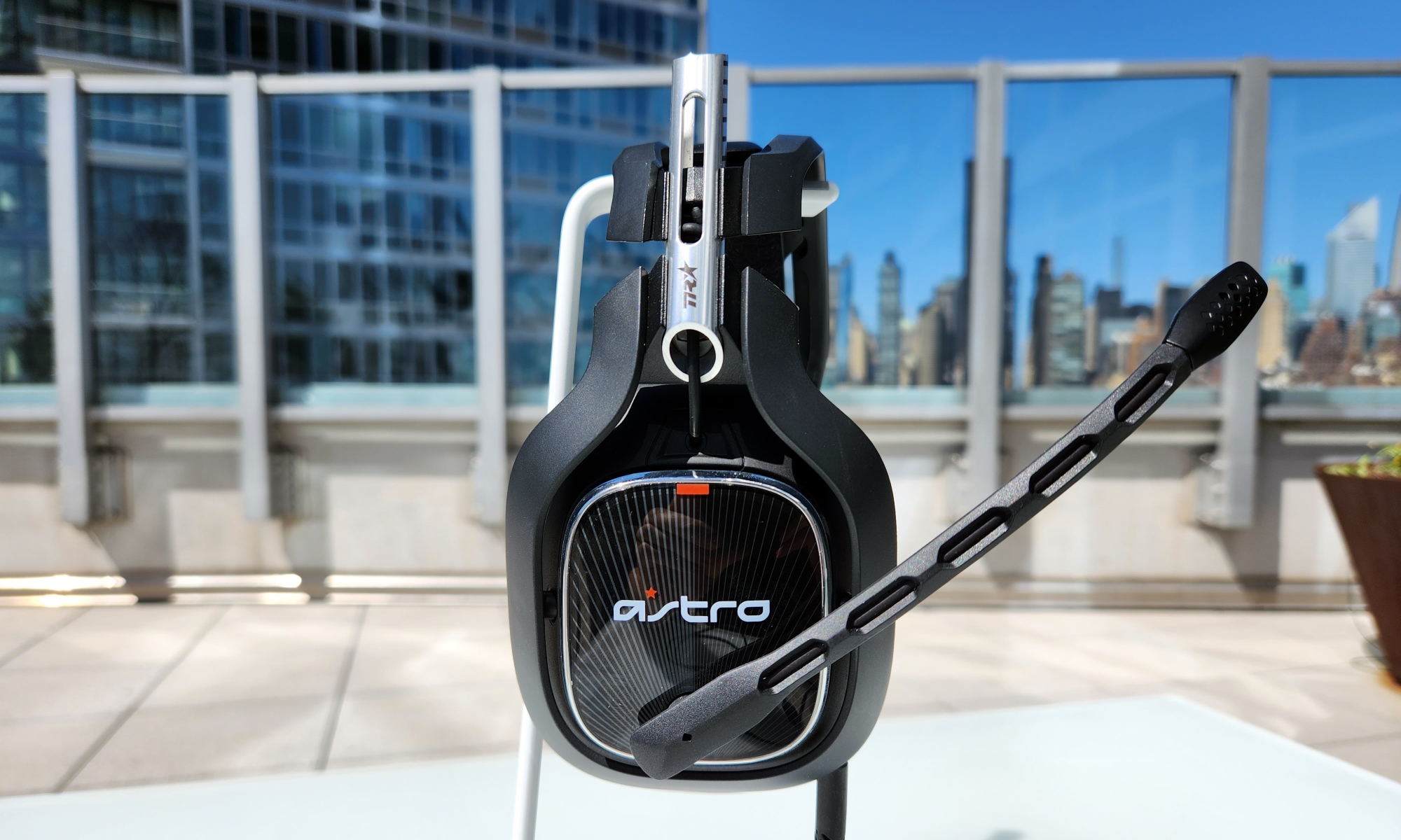 The Astro A40 TR gaming headset rests on a white stand on an outside table, with its built-in microphone extended.