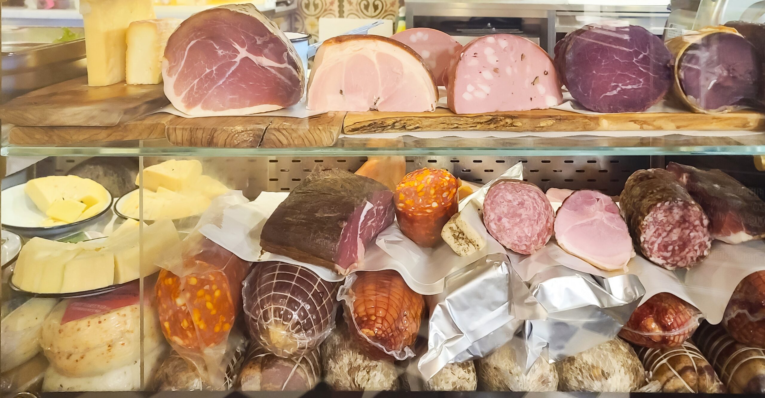 This is a view into a display case at a prosciutteria in Venice, Italy. The case is full of traditional cured meats as well as a selection of cheeses, viewed mostly in cross-section.