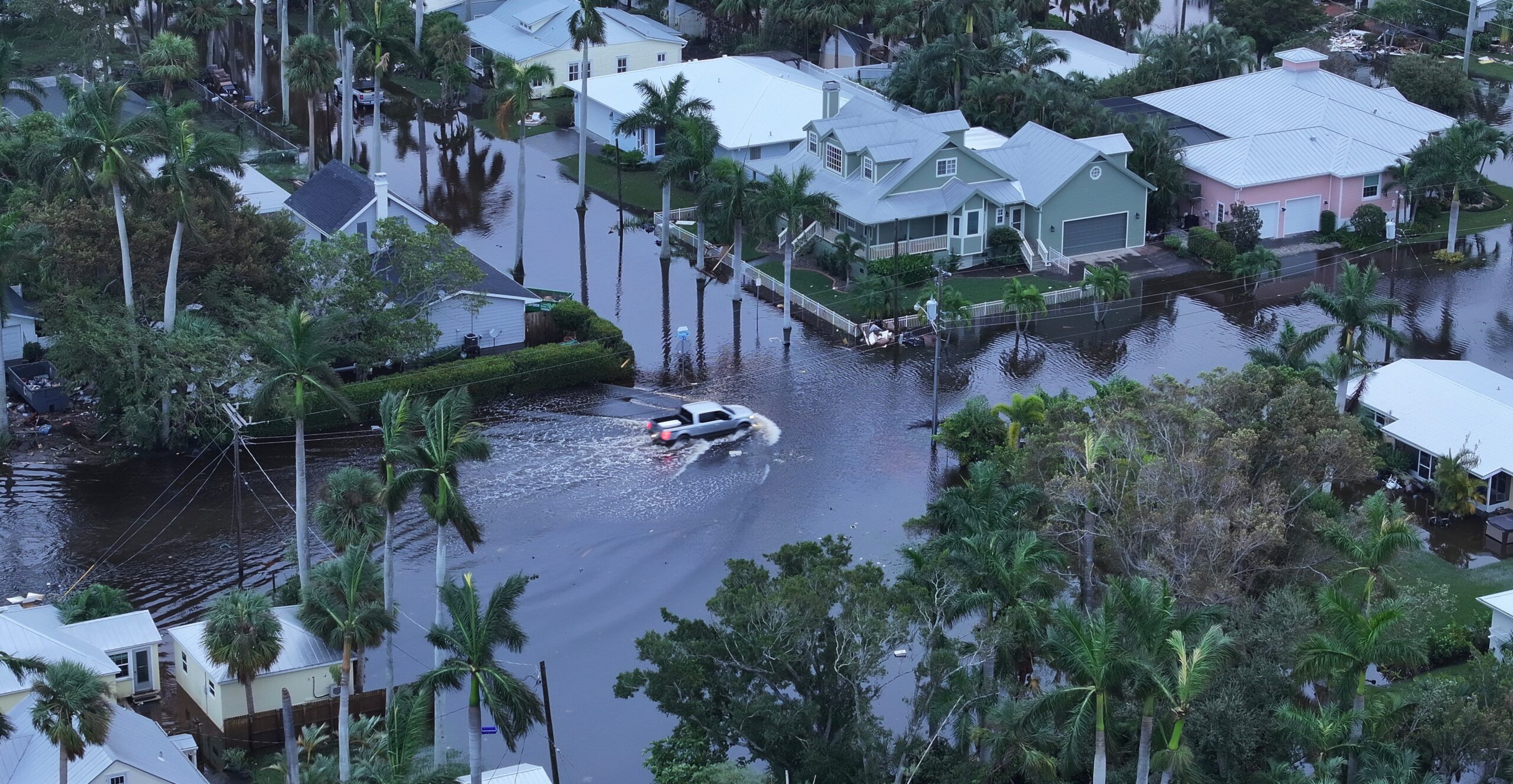 Aerial photo of a flooded neighborhood with a pickup truck driving down a flooded street.