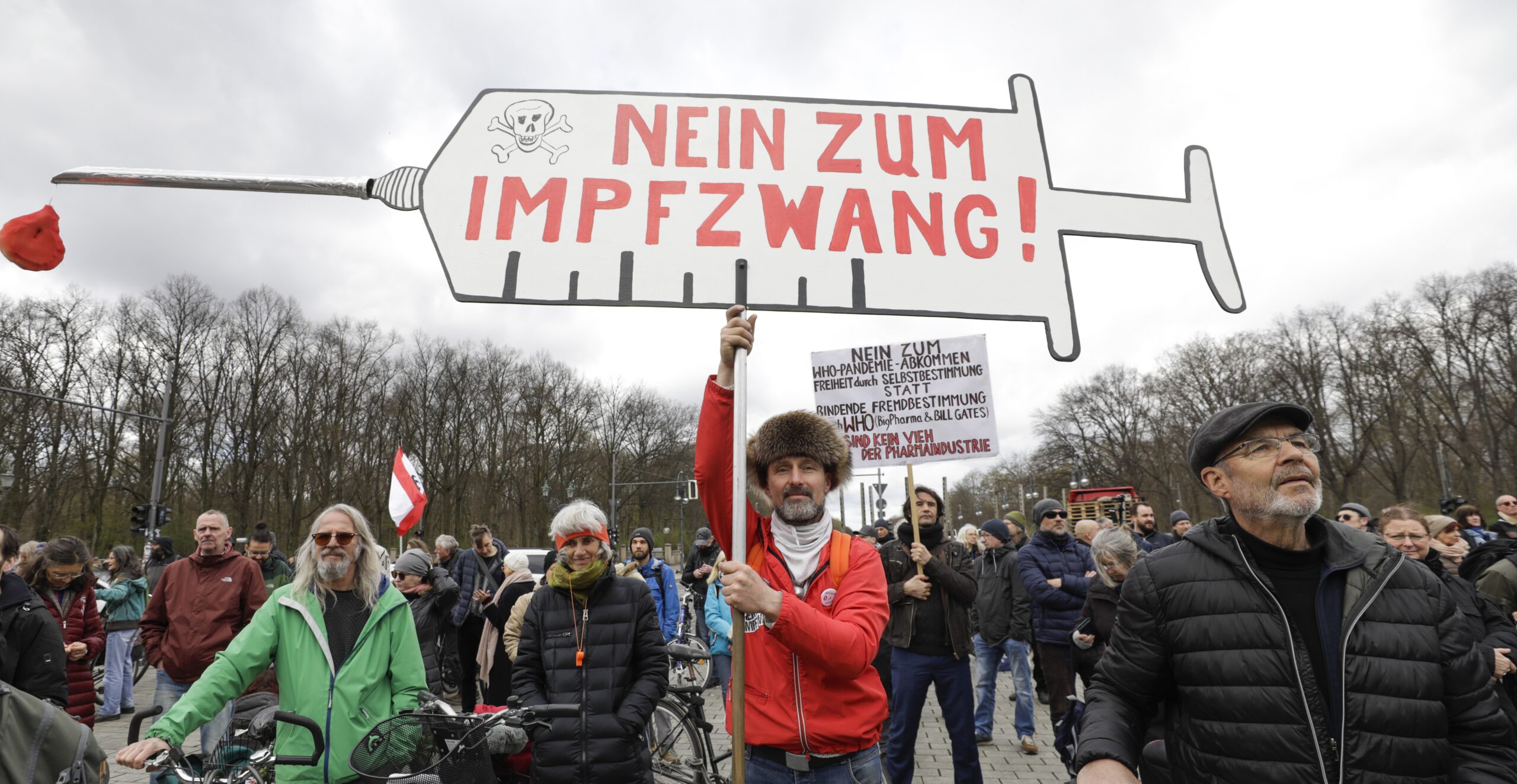 A crowd of demonstrators hold up signs written in German protesting against compulsory vaccination.