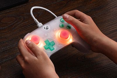 The 8BitDo Ultimate Mini controller being held in two hands with its joysticks glowing.