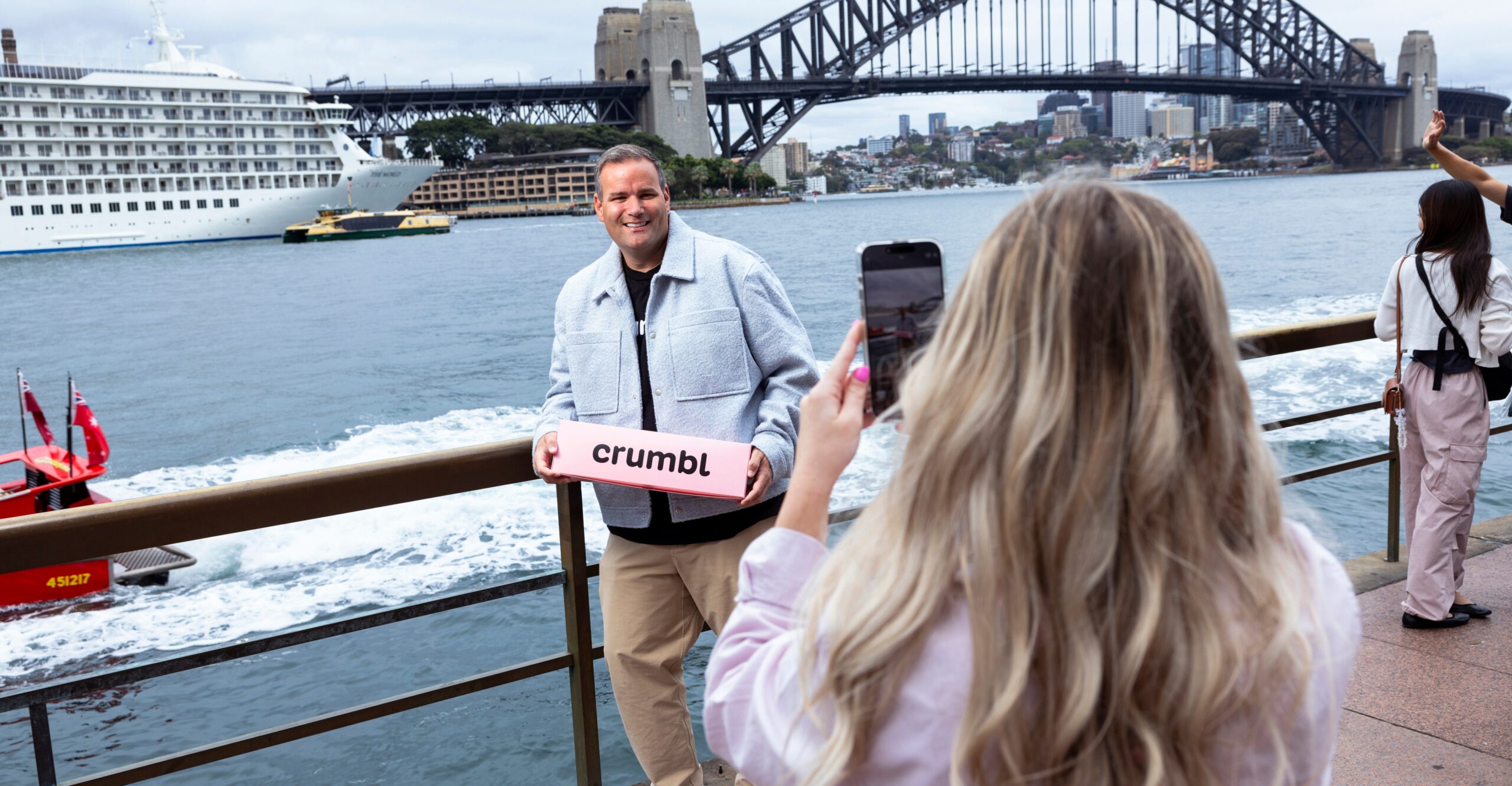 McGowan holding a pink Crumbl box posing by the water as someone takes his photo.