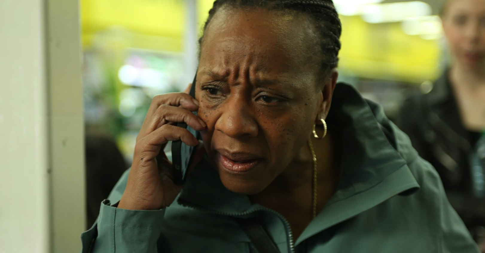 An older Black woman frowns as she holds a phone to her ear.