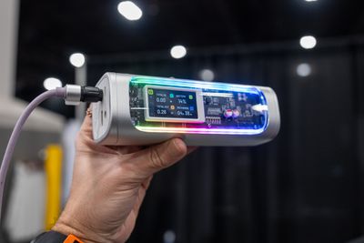 A see-through power bank with RGB lighting held in-hand at a trade show.