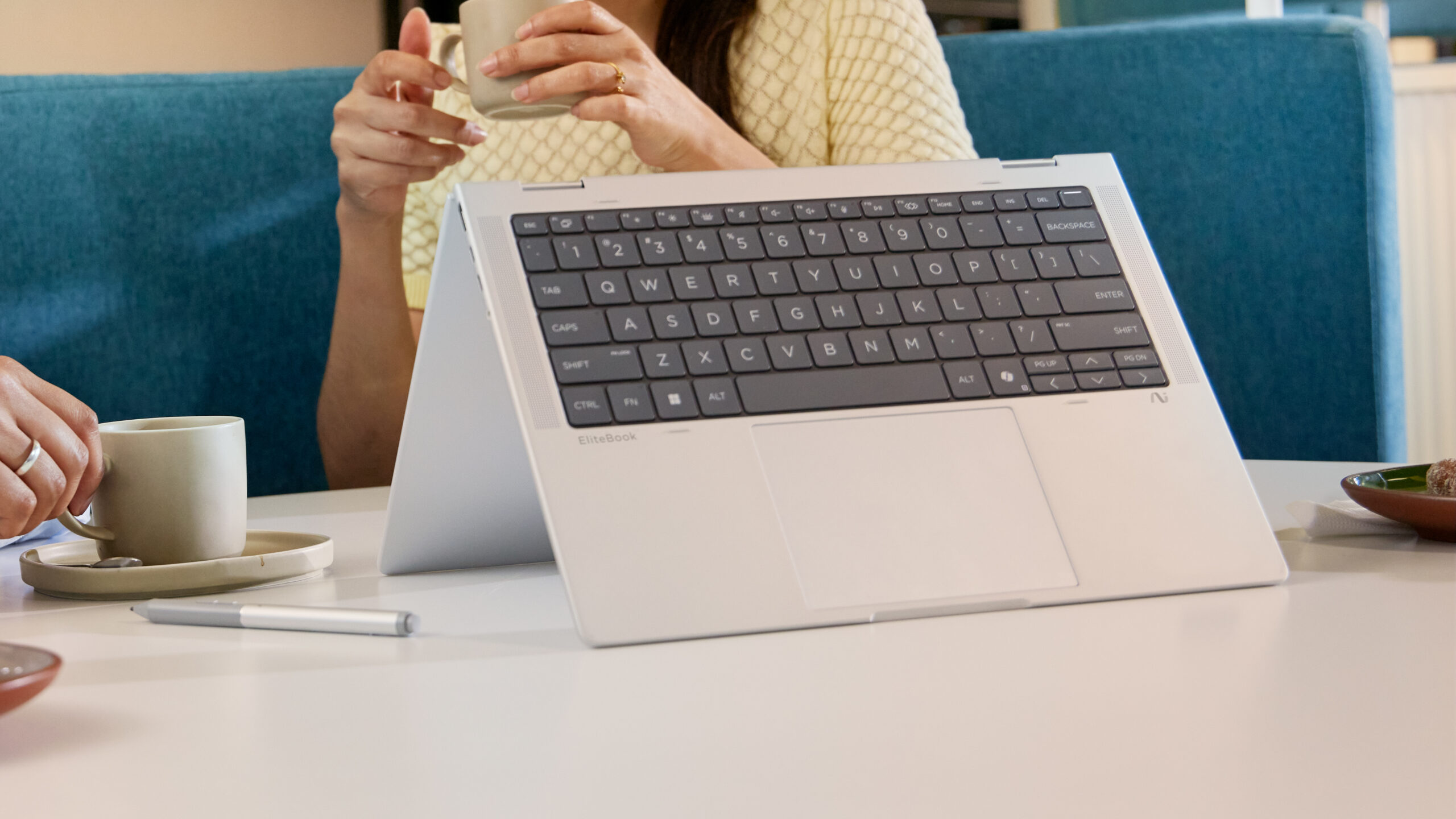 Product lifestyle image of the HP EliteBook X Flip G1i. It sits, folded in tent mode, on a diner coffee table.