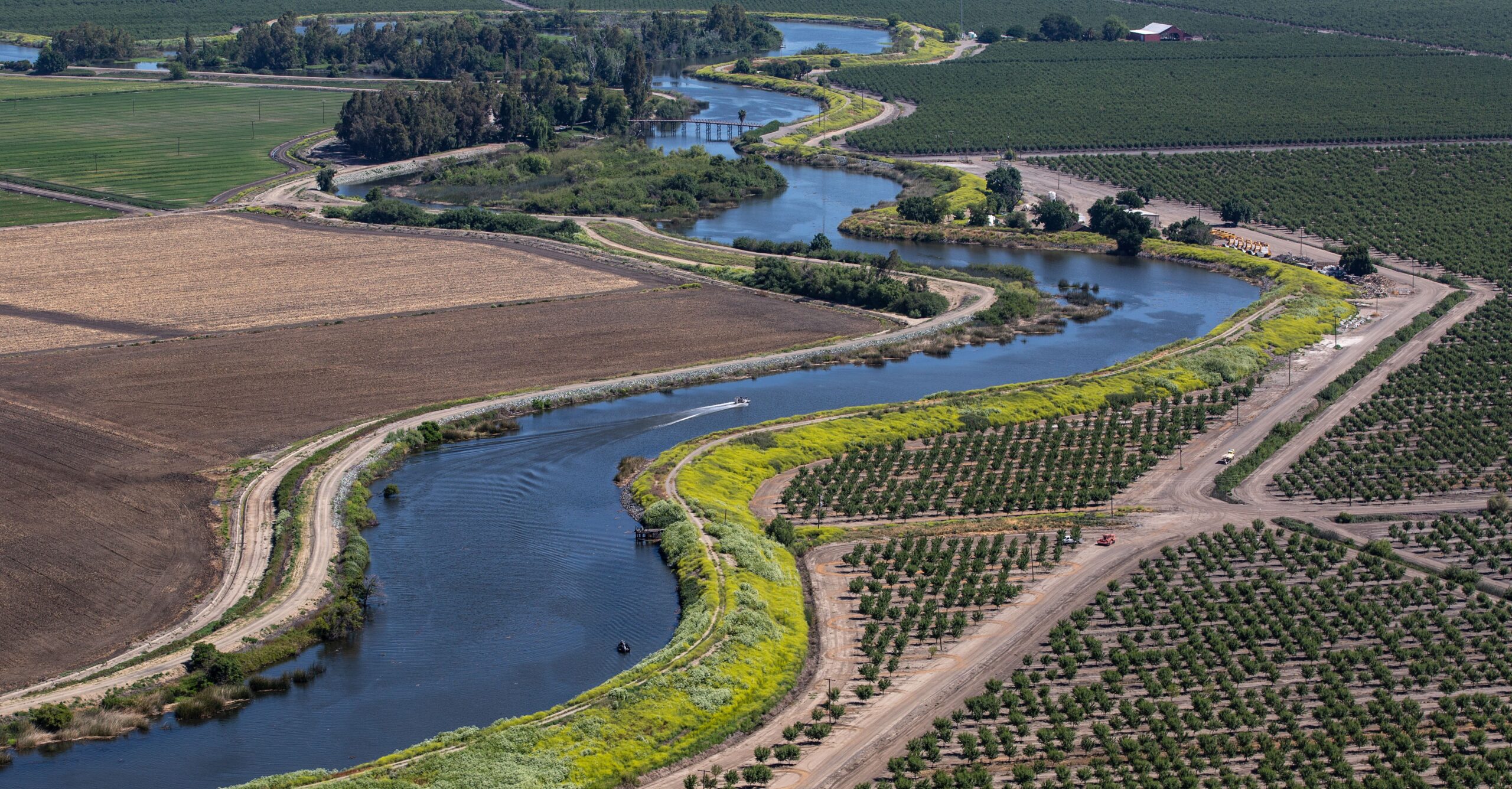 An aerial view of a river snaking through green and brown sections of farmed land.