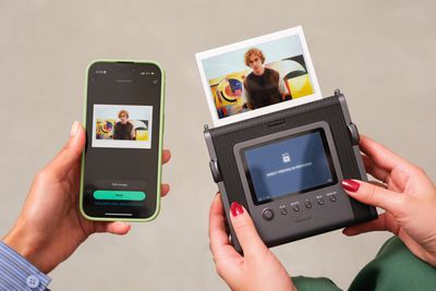 The Fujifilm Instax Wide Evo Hybrid camera next to a smartphone running an app it’s wirelessly connected to.