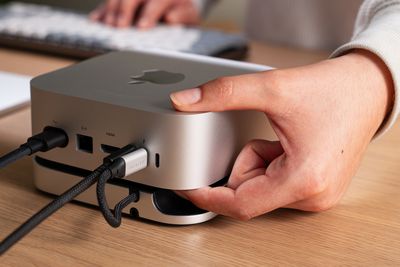 A person accessing the Mac Mini M4’s power button through a cut-out on Satechi’s hub sitting on a desk.