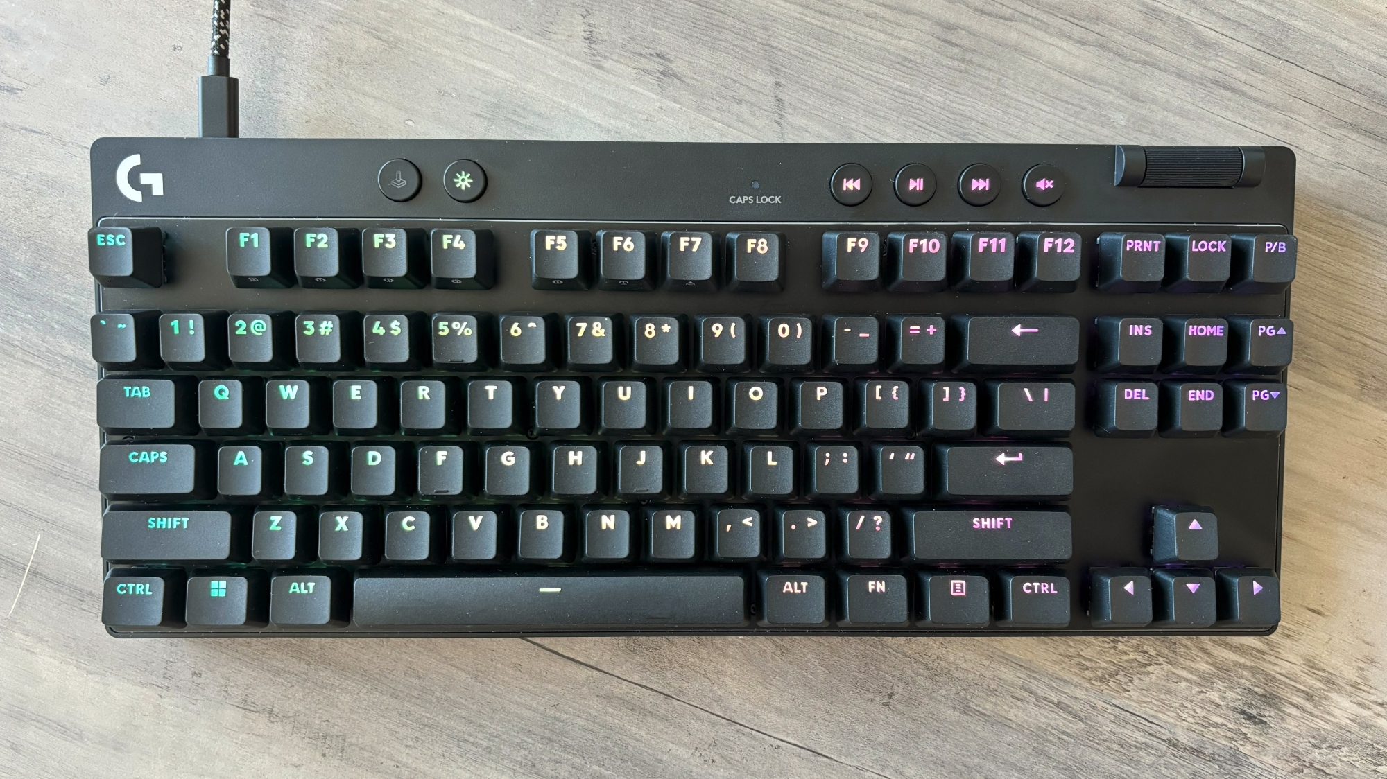 A black gaming keyboard, the Logitech G Pro X TKL Rapid, rests on a brown wooden table.