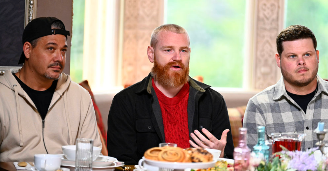 Three men sit at a table full of food.