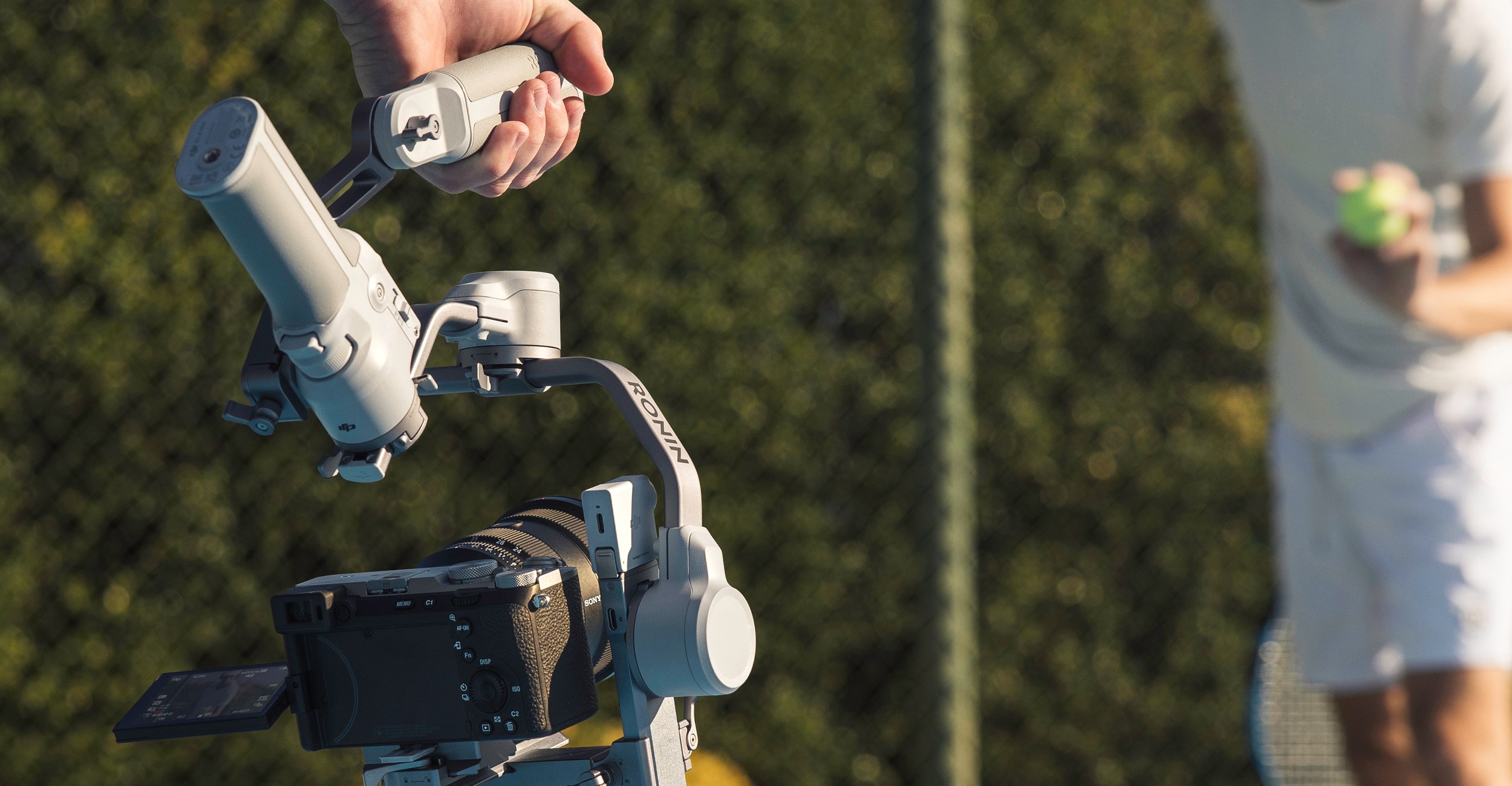 A person is filming a tennis player using the DJI RS 4 Mini’s optional briefcase handle accessory.