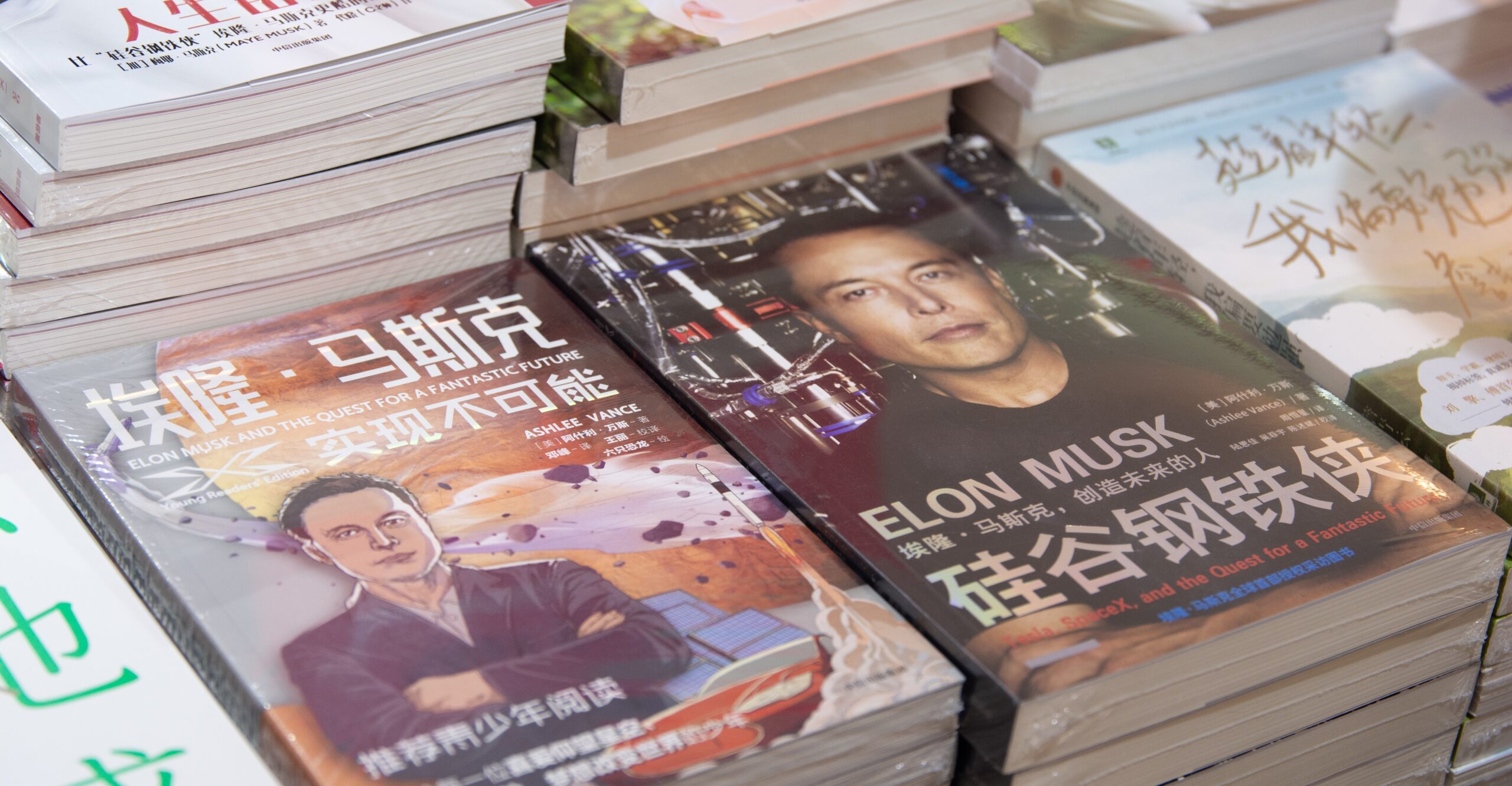 Stacks of books in Chinese with Elon Musk on the cover are piled on a table.