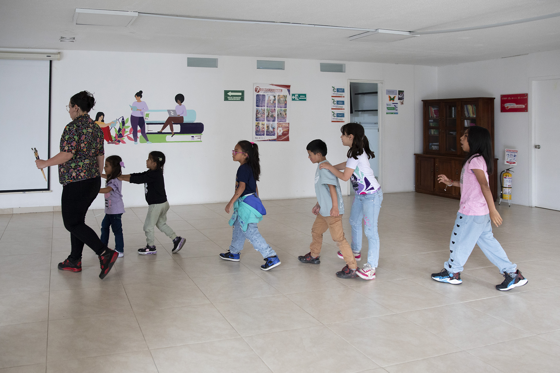 an instructor leads a line of six children through the lobby of a care block building