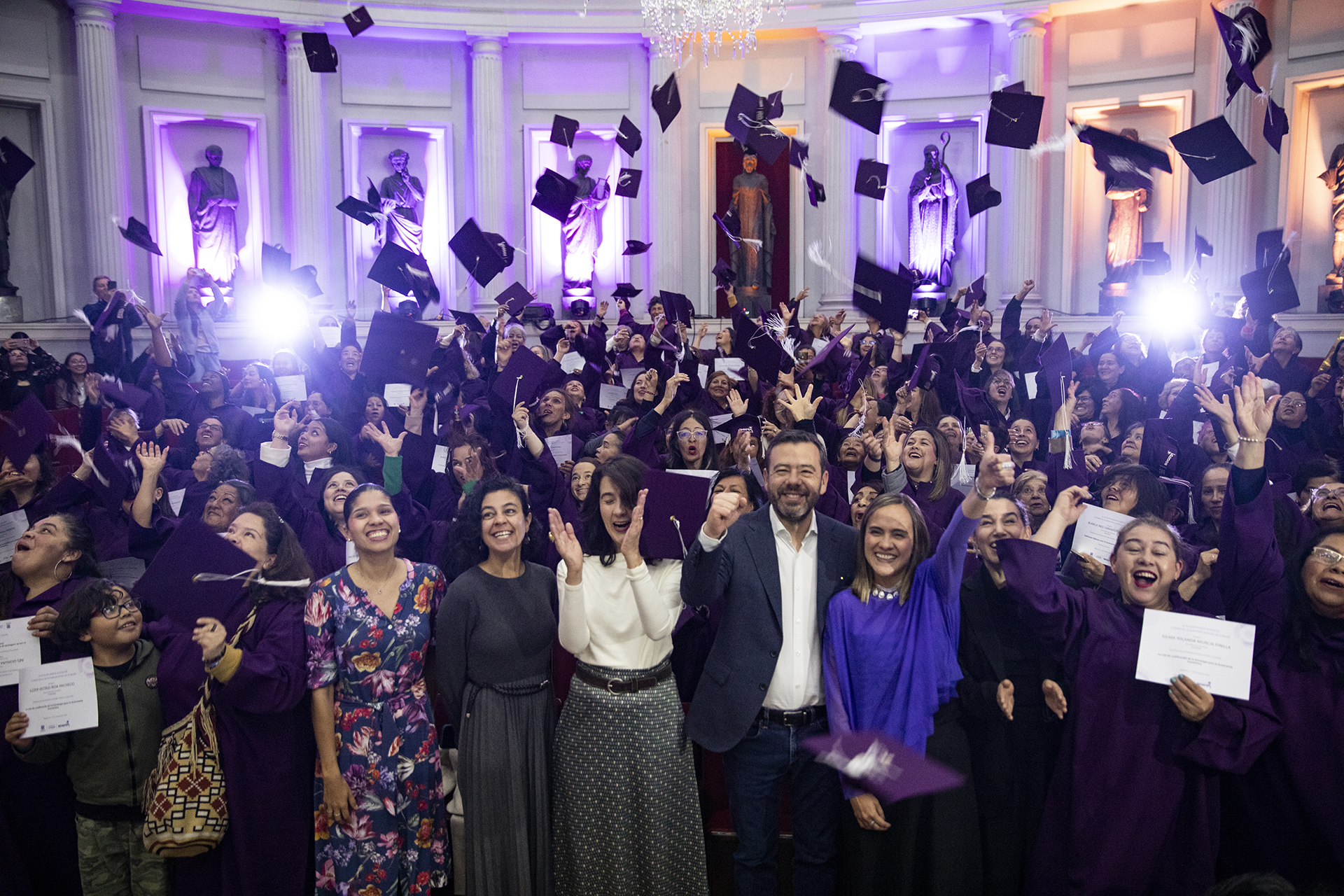 a room filled with people in graduation gowns throwing their caps in the air and cheering