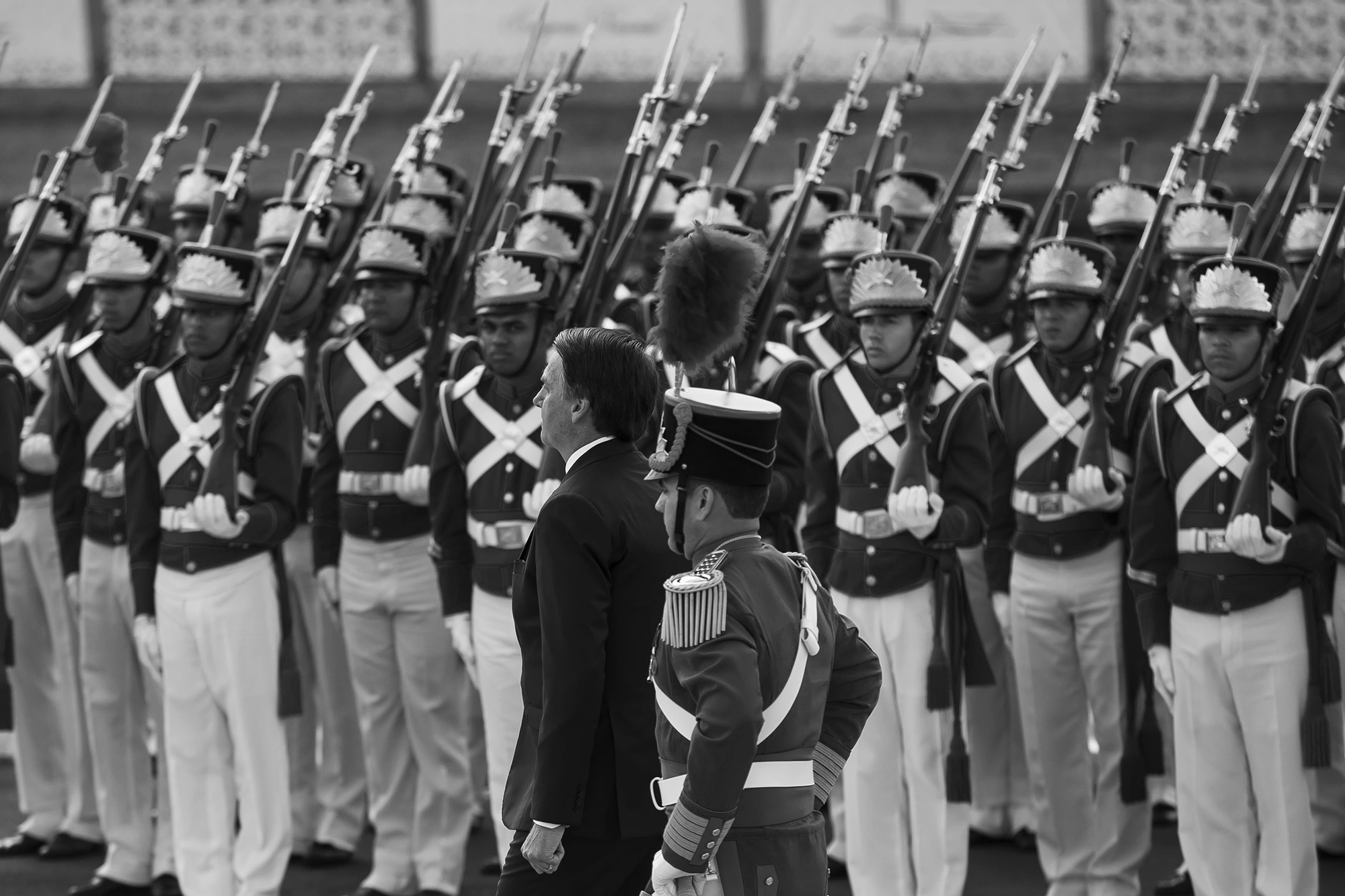 Soldiers in dress uniforms stand at attention as Bolsonaro passes.