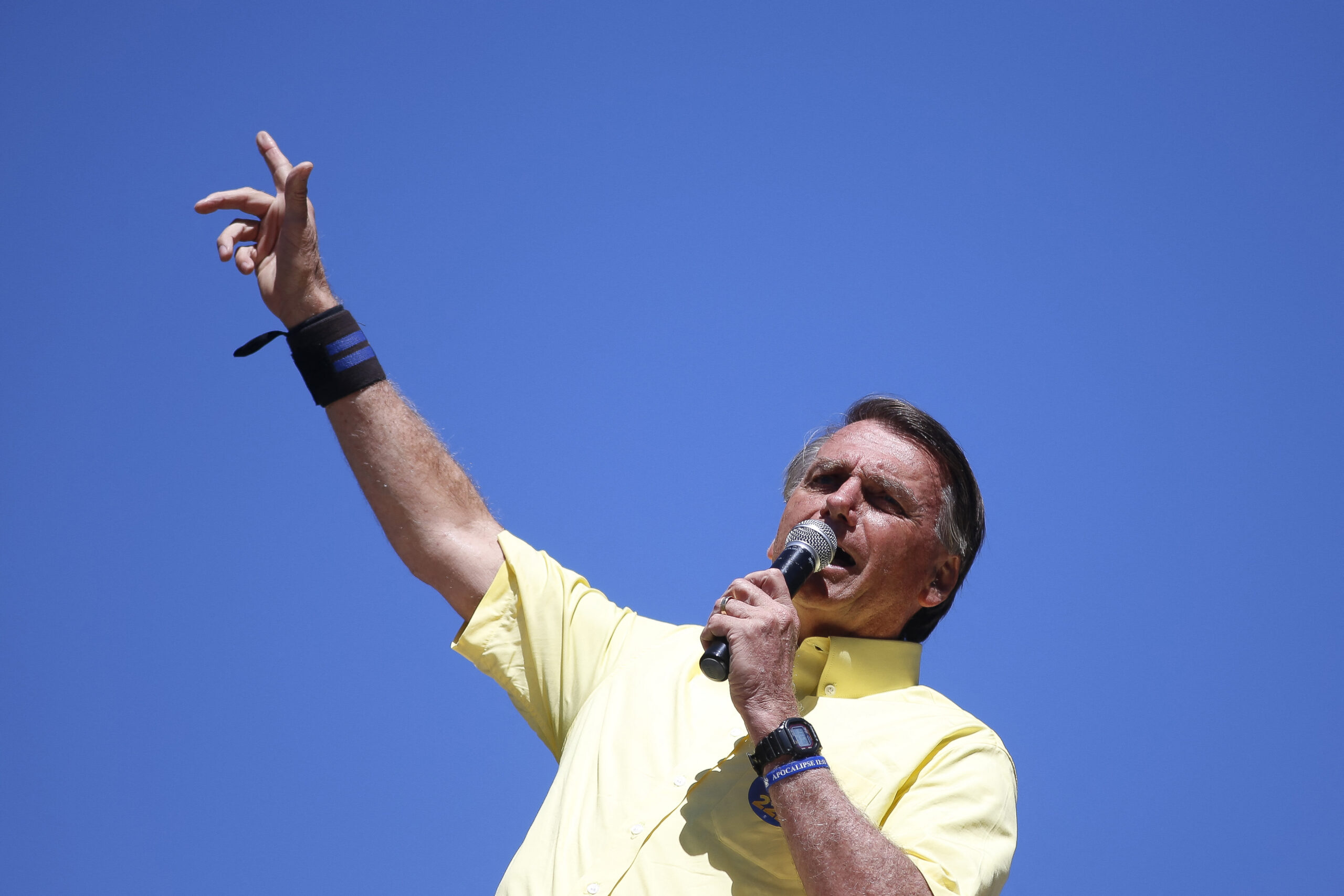 Bolsonaro speaks into a microphone and raises one hand in the sky