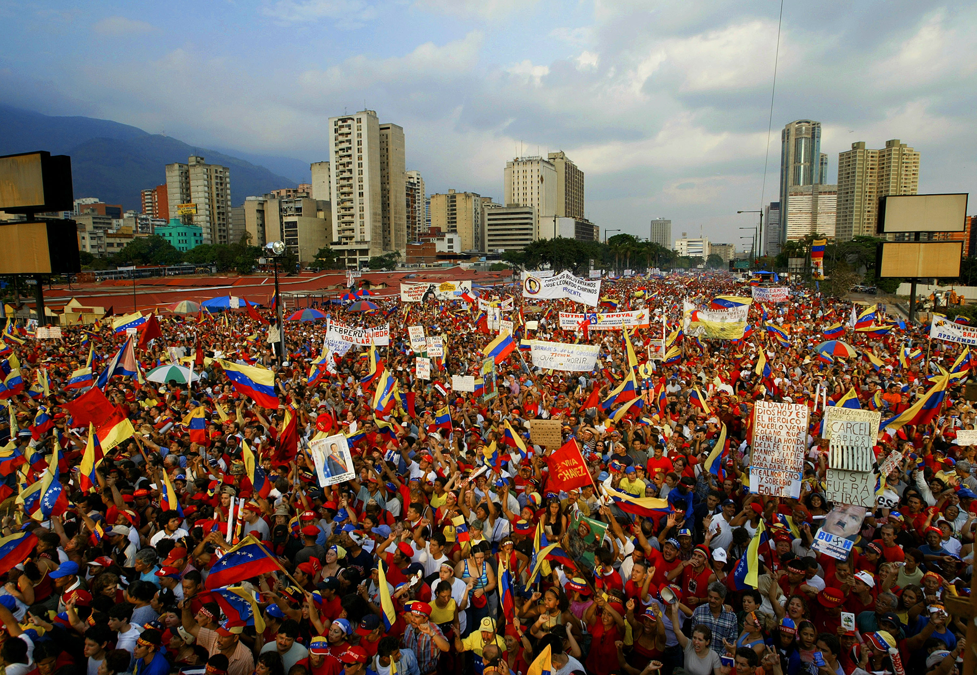 A massive crowd of people holding signs and Venezuelan flags outside