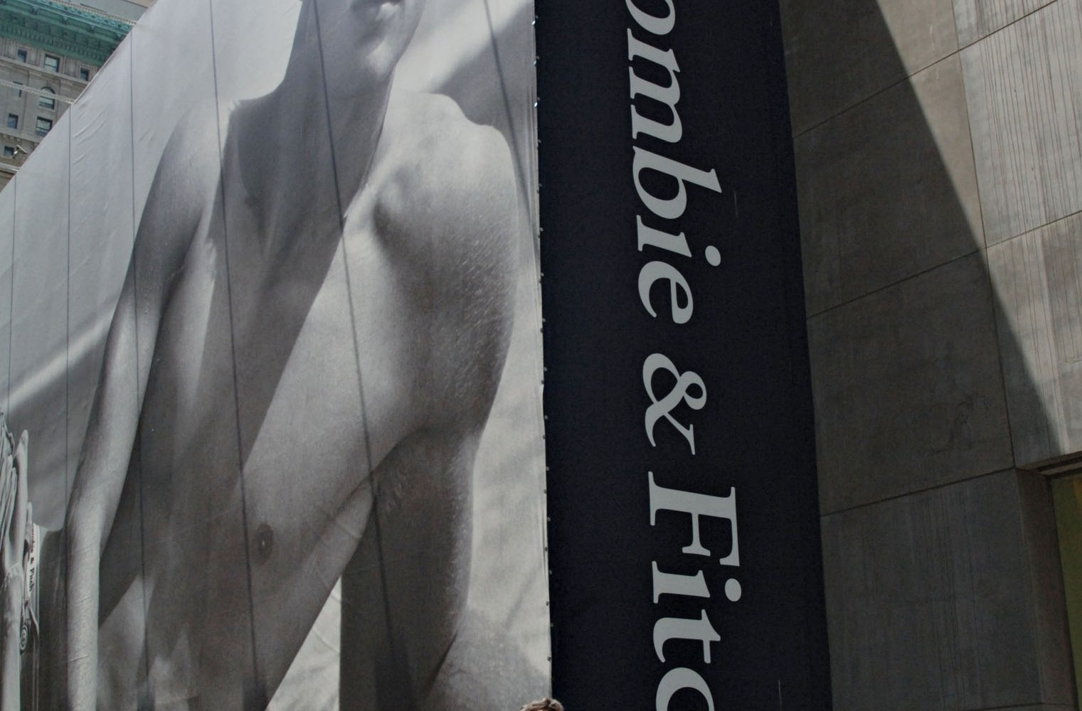 A streetcorner billboard shows a black-and-white photo of a shirtless man. A streetcorner billboard shows a black-and-white photo of a shirtless man.