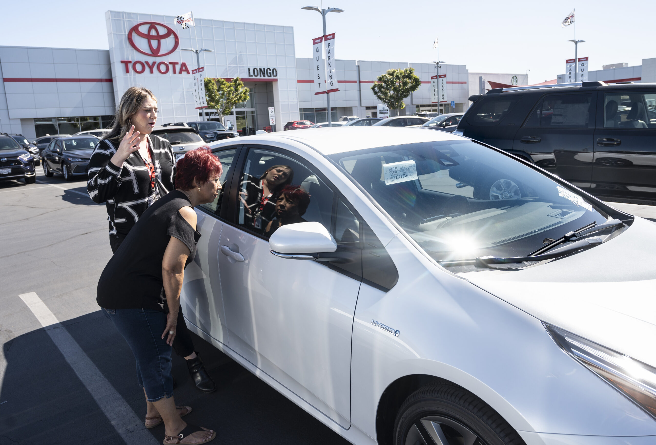 a customer is shown a 2022 white toyota prius car at a toyota dealership lot outdoors
