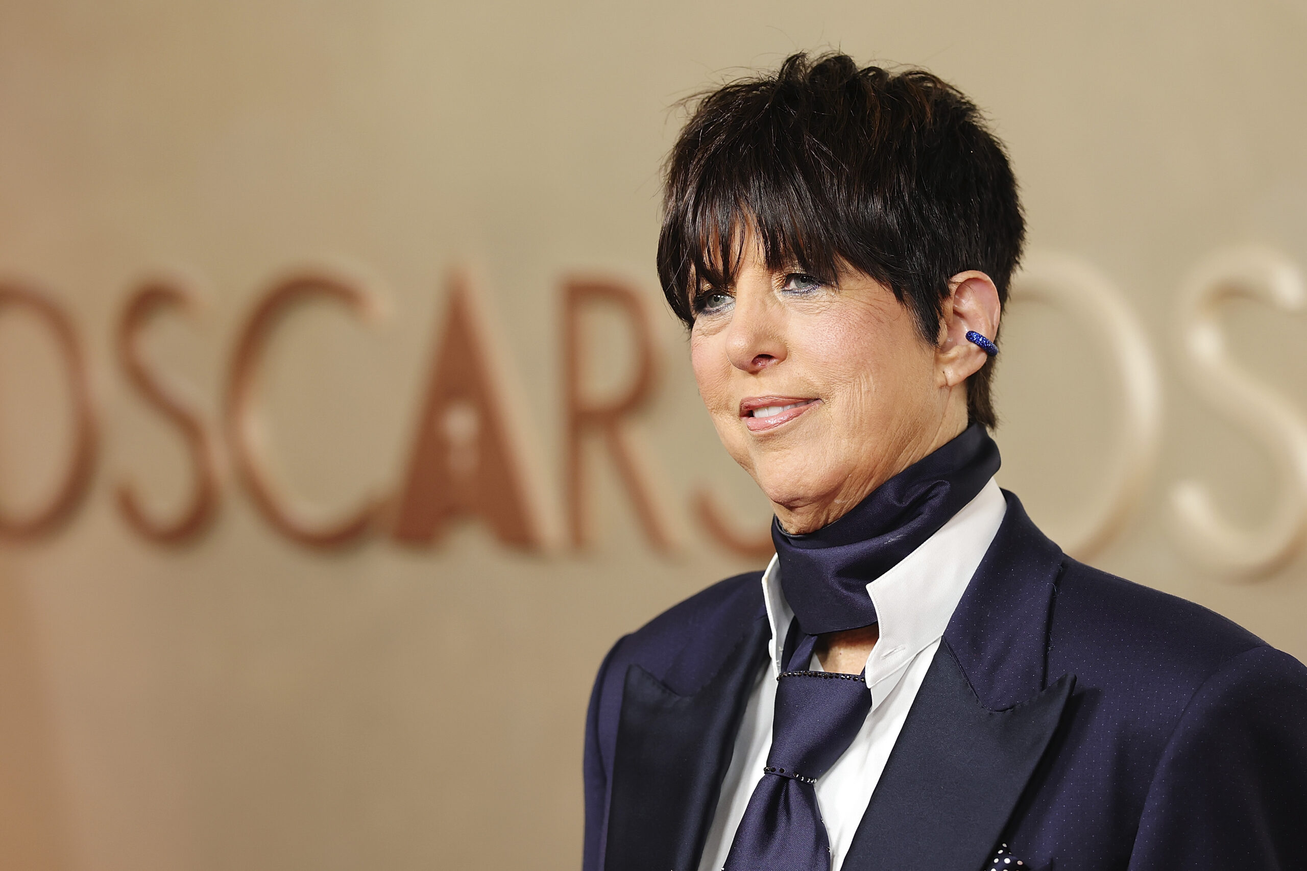 Songwriter Diane Warren, in a navy silk scarf, suit and tie with short black hair, at the Oscars.