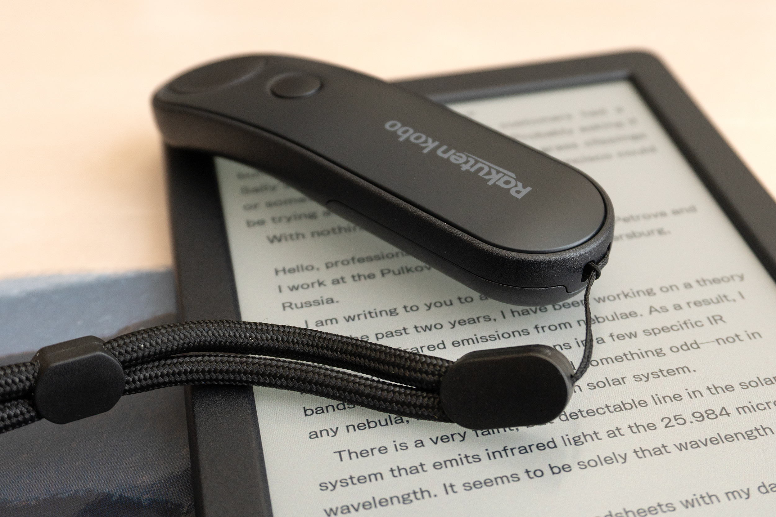 The Kobo Remote with a lanyard attached sitting on a Kobo e-reader.