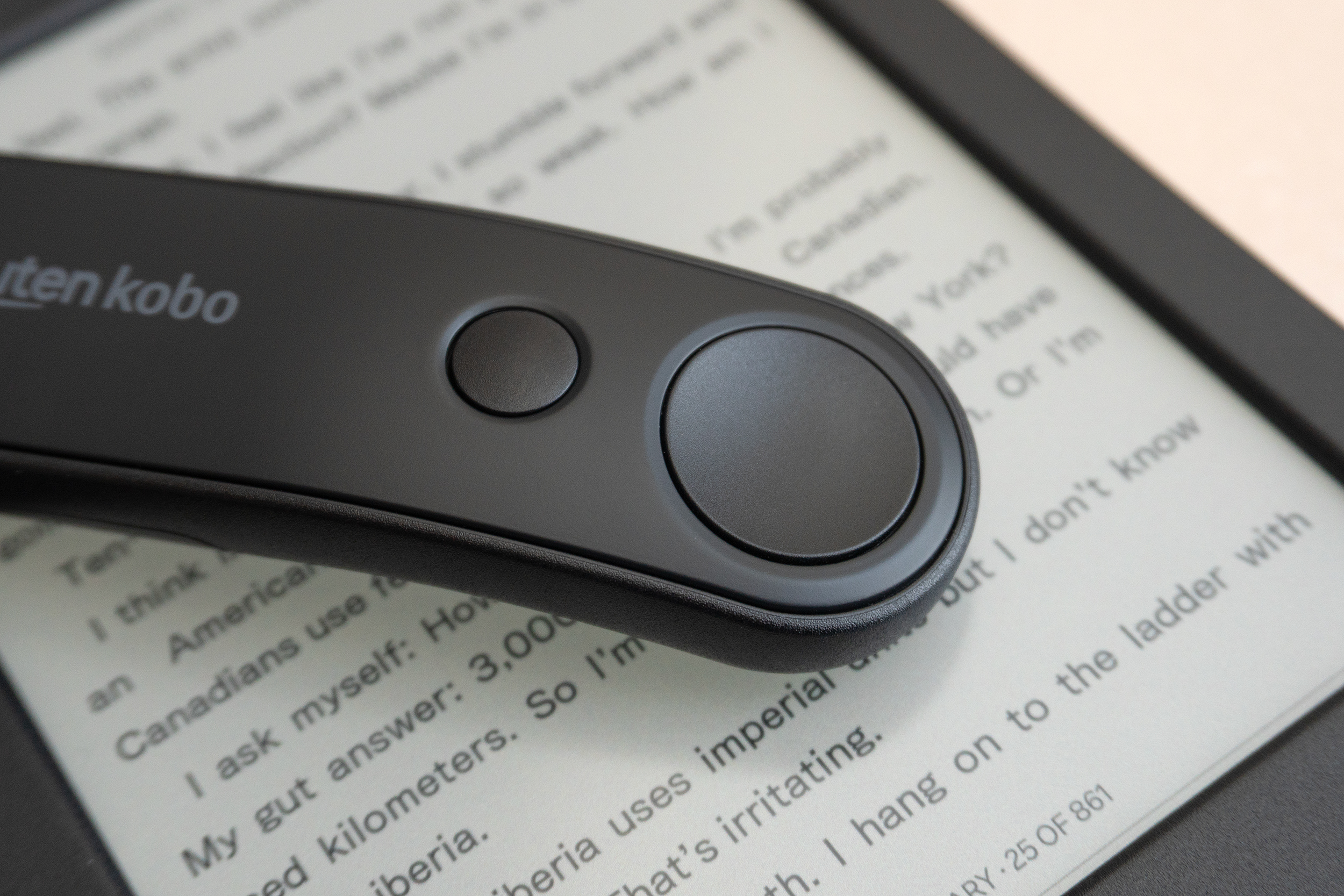 A close-up of the page turn buttons on top of the Kobo Remote sitting on a Kobo e-reader.