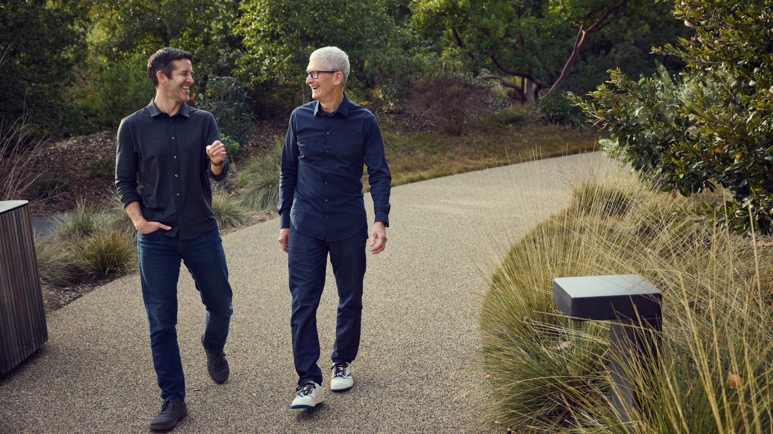 John Ternus and Tim Cook shown walking side by side on a path, smiling at each other