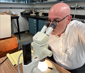 Robert J. Madden examines artifacts under a microscope in a laboratory setting.