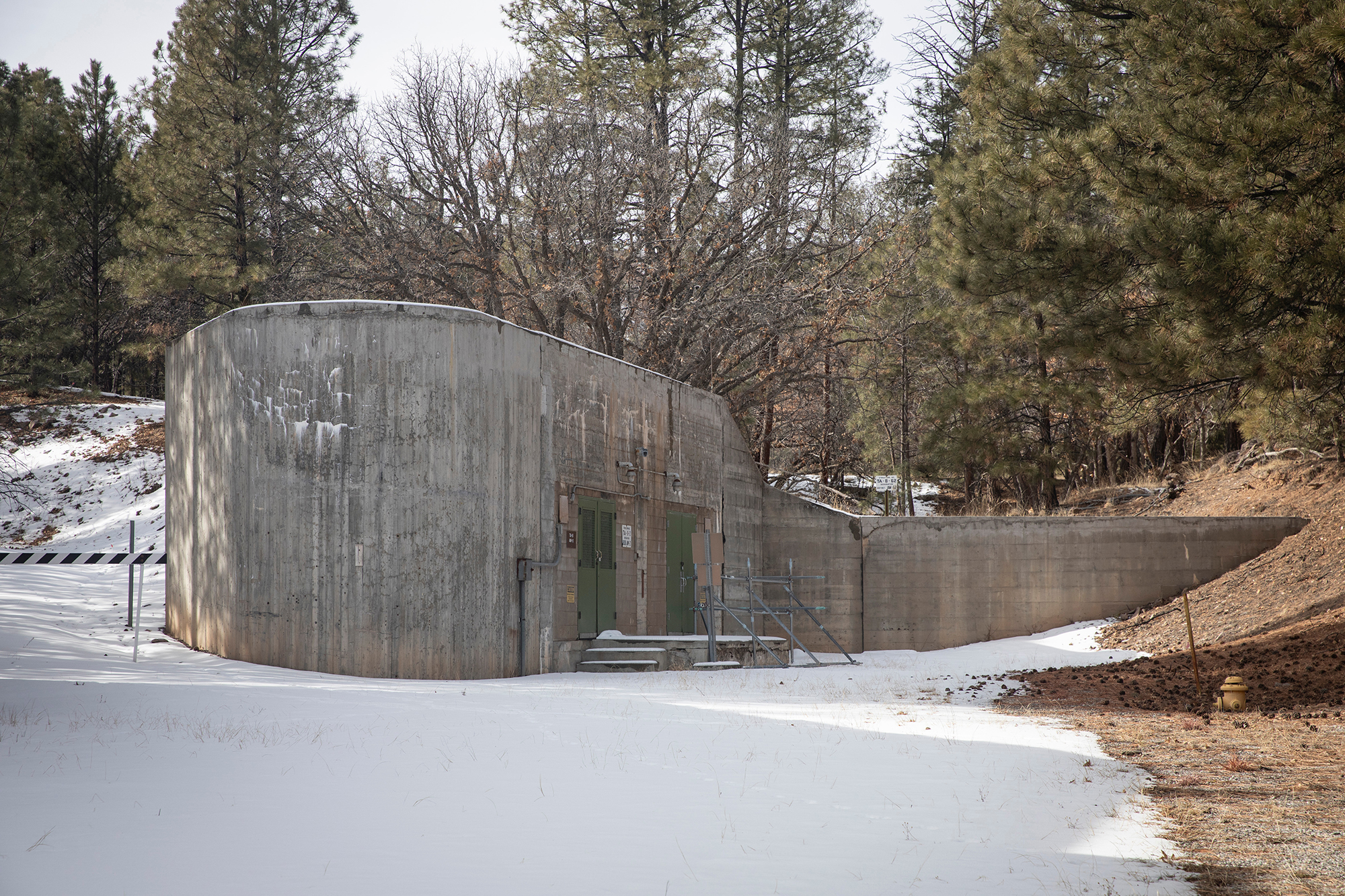 the snowy exterior of a windowless, concrete building backed up to forest the snowy exterior of a windowless, concrete building backed up to forest