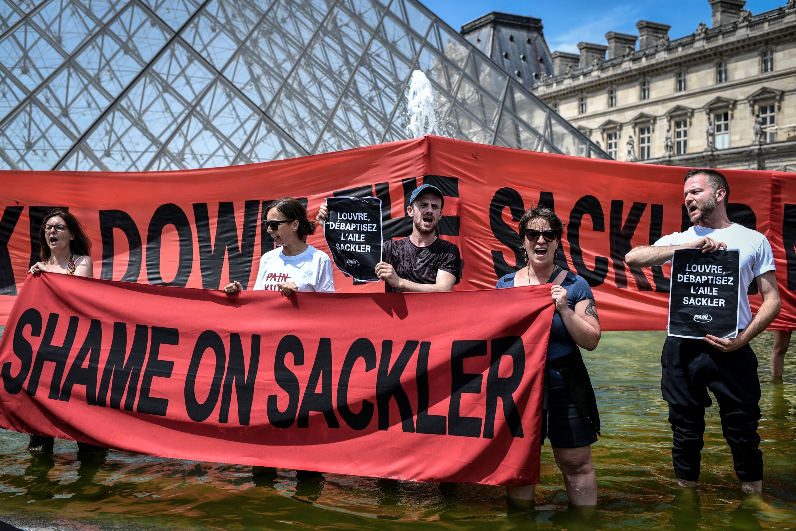 Protesters stand outside of the Louvre holding a red sign saying ‘Shame on Sacklers’