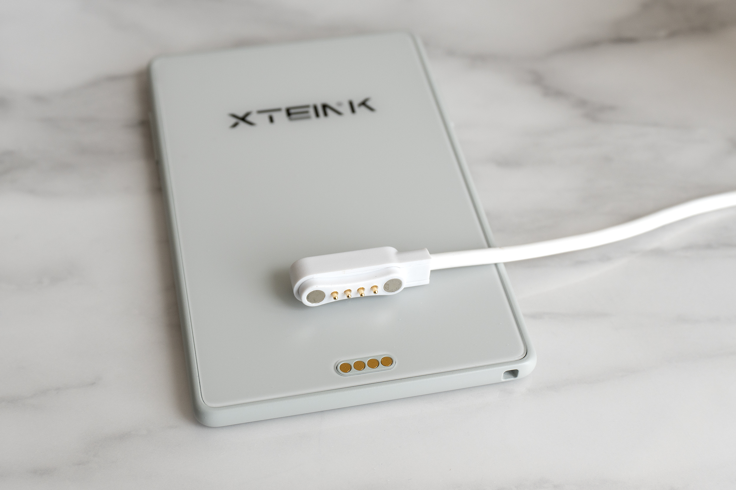 A proprietary charging cable laying on the back of the Xteink X3 e-reader.