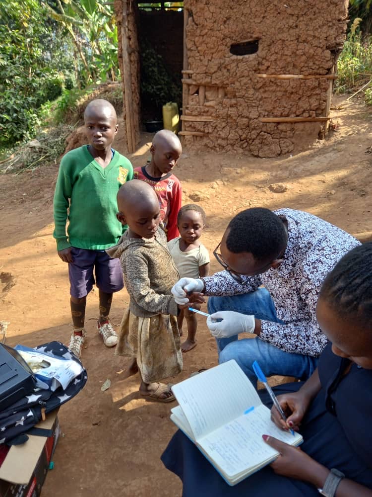 Two health workers test children while writing notes in a notebook on a dirt road. Two health workers test children while writing notes in a notebook on a dirt road.