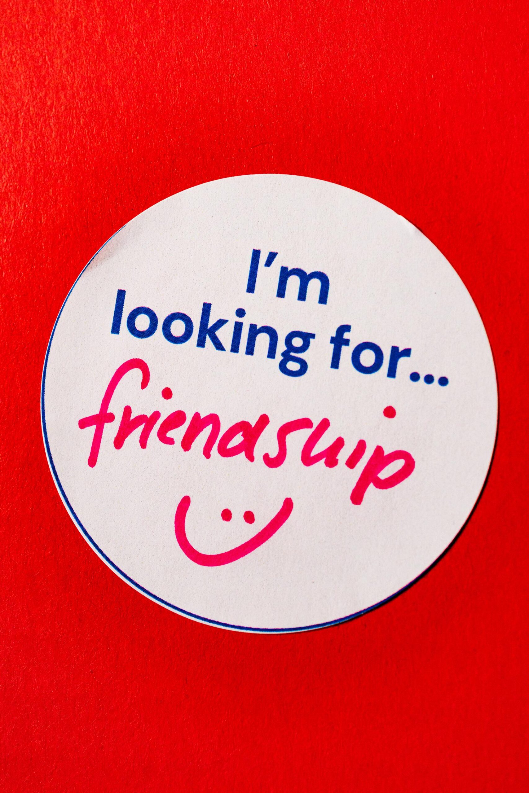 a sticker reading “I’m looking for… friendship” with a hand-drawn smiley face is stuck to a red wall