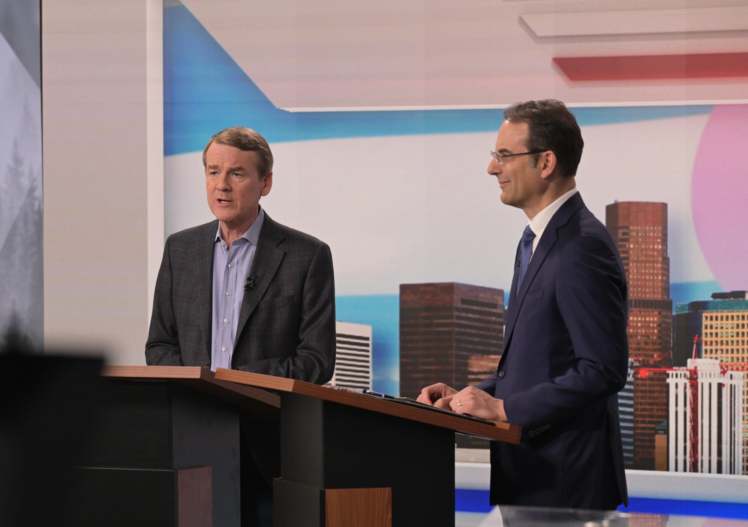 Sen. Michael Bennet, left, and Attorney General Phil Weiser stand behind separate podiums at a TV studio Sen. Michael Bennet, left, and Attorney General Phil Weiser stand behind separate podiums at a TV studio