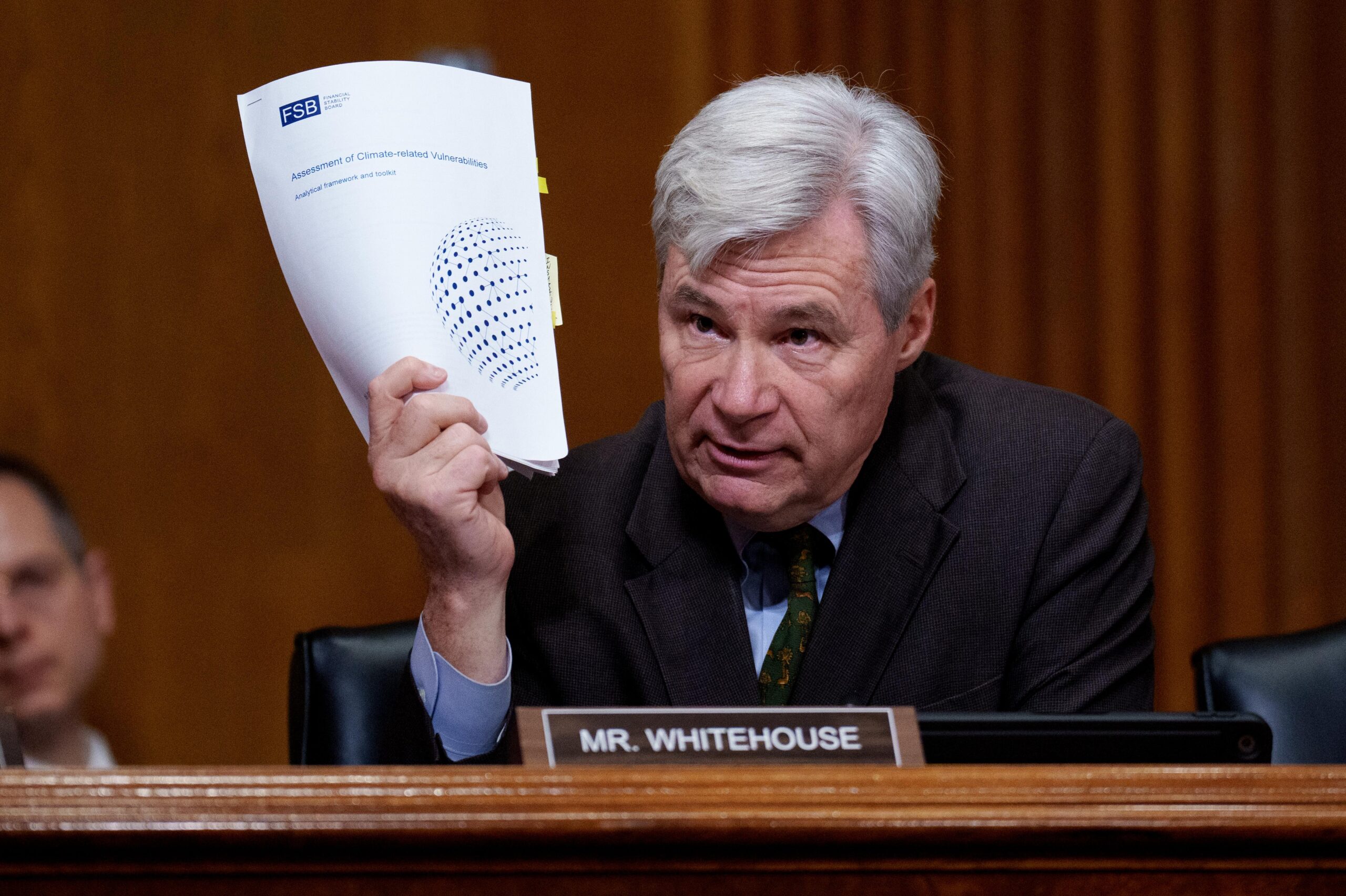 Sen. Sheldon Whitehouse holds up a document titled "Assessment of Climate-related Vulnerabilities" as he speaks during a Senate Committee hearing