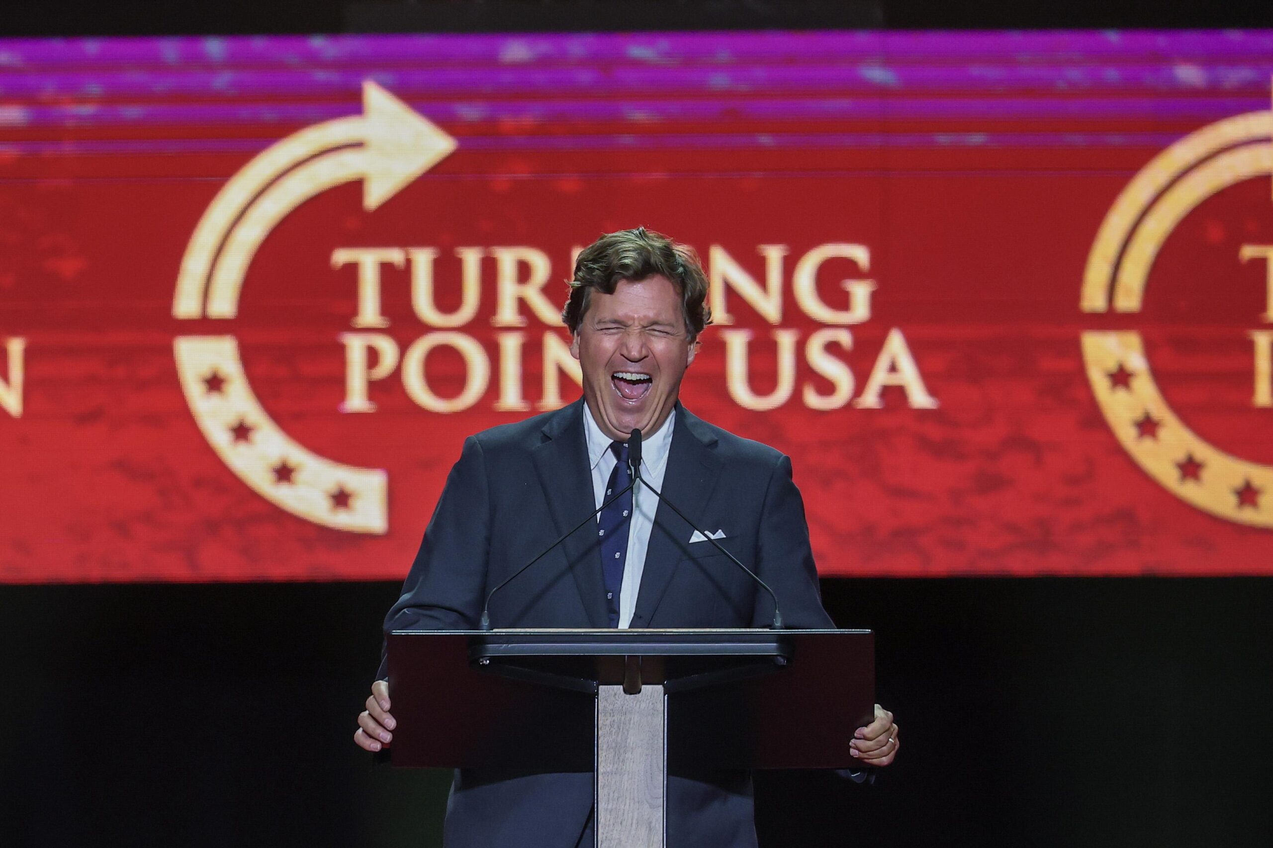 Tucker Carlson at a podium for a TPUSA event