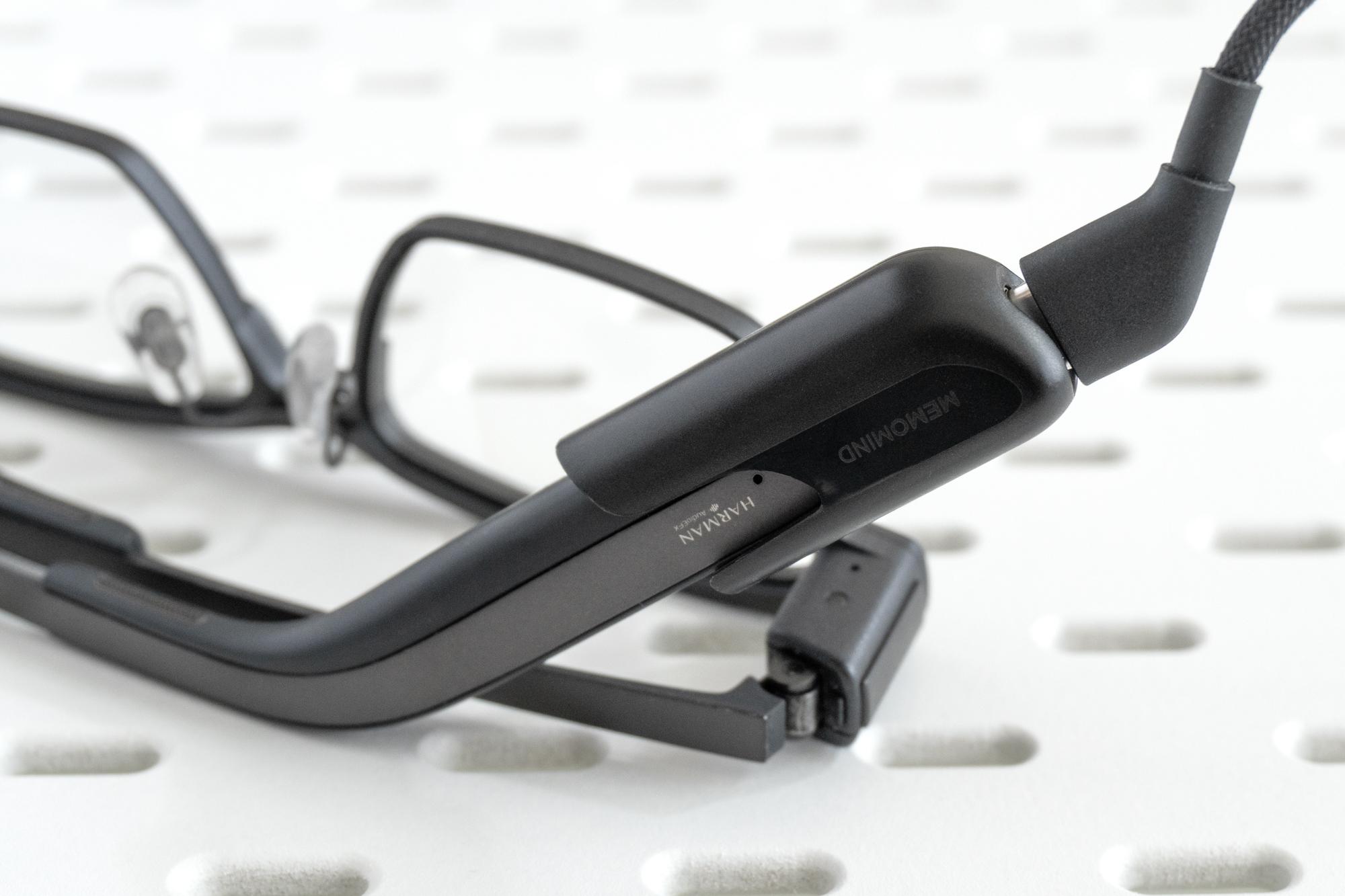A USB-C cable attached to a charger connected to the end of one of the MemoMind One glasses’ arms.