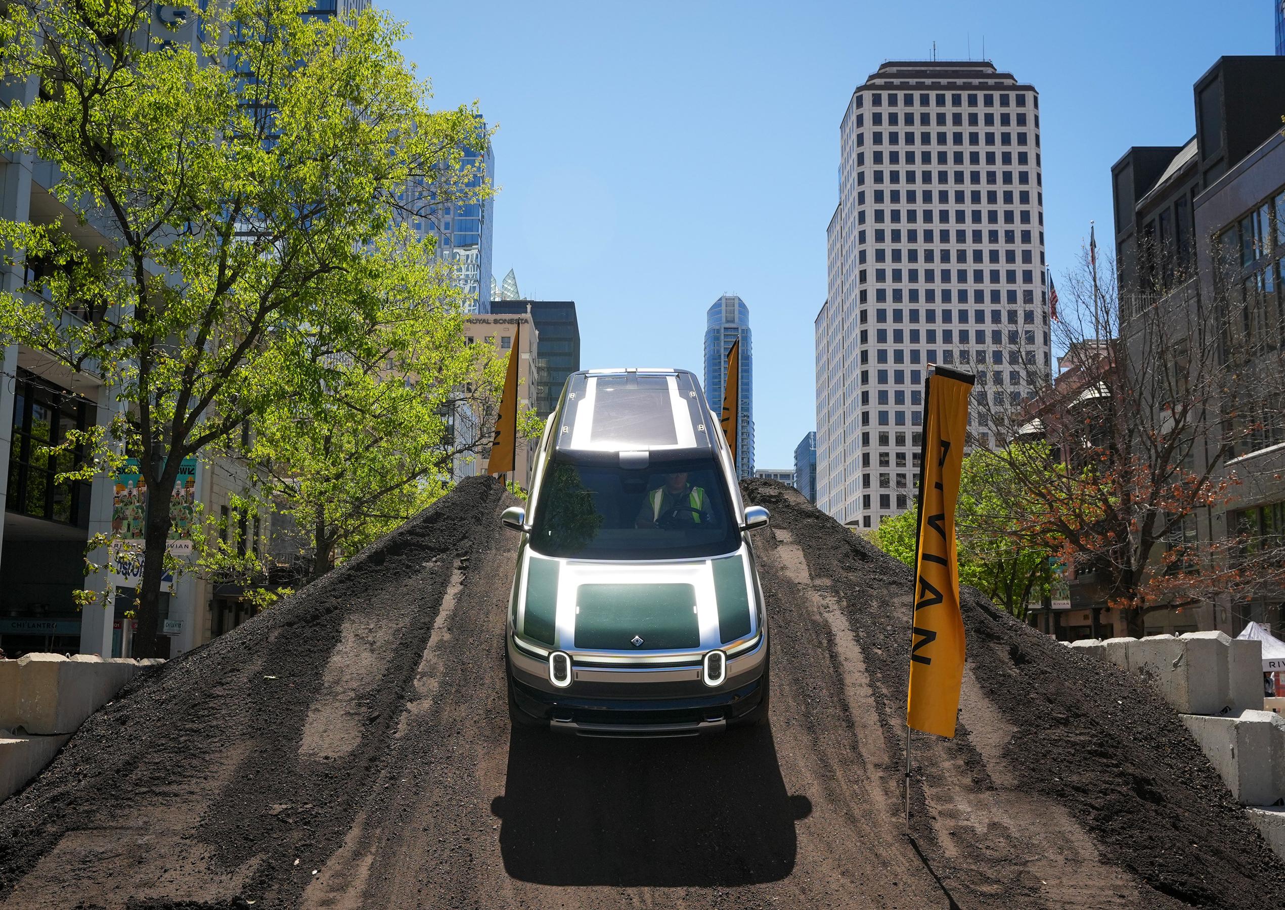 A Rivian R2 with a green hood is displayed on top of a large dirt mound in the city center as part of an activation for South by Southwest. A Rivian R2 with a green hood is displayed on top of a large dirt mound in the city center as part of an activation for South by Southwest.