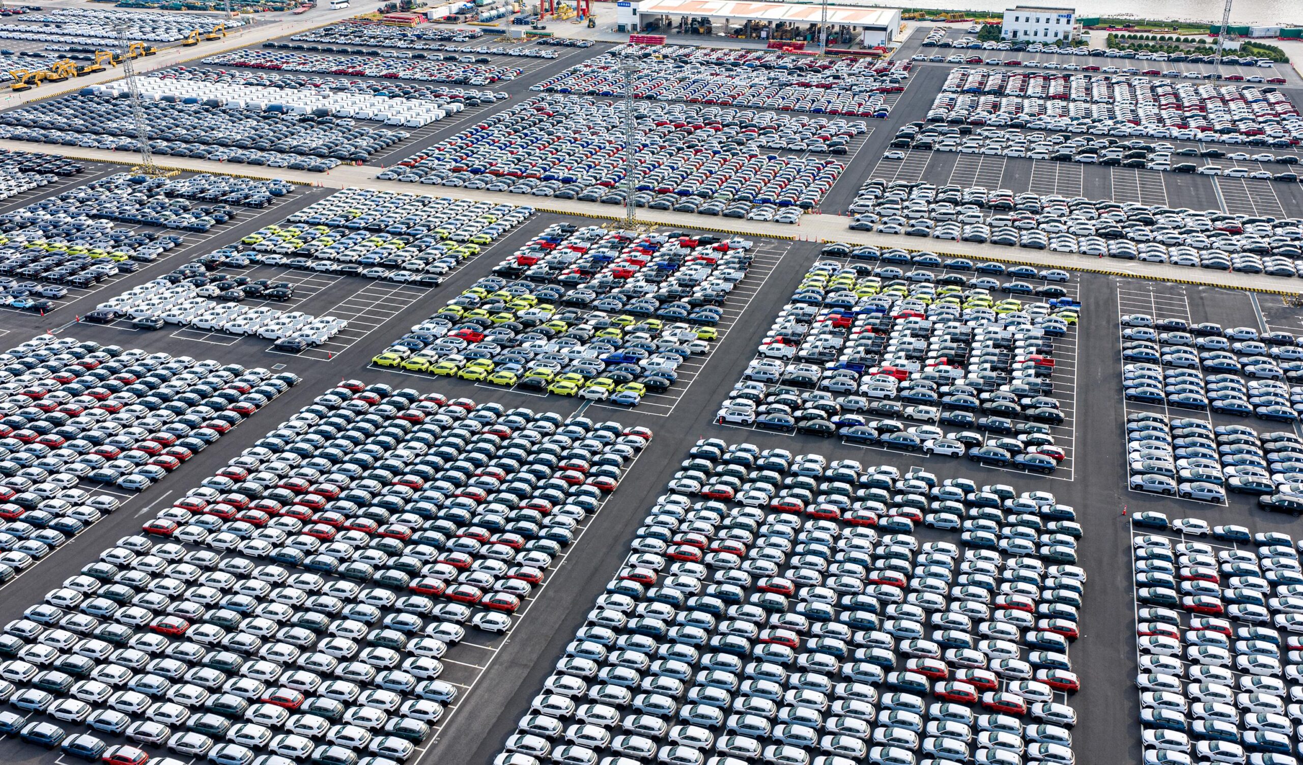Hundreds of cars neatly arranged can be seen in an enormous parking lot from above. Hundreds of cars neatly arranged can be seen in an enormous parking lot from above.