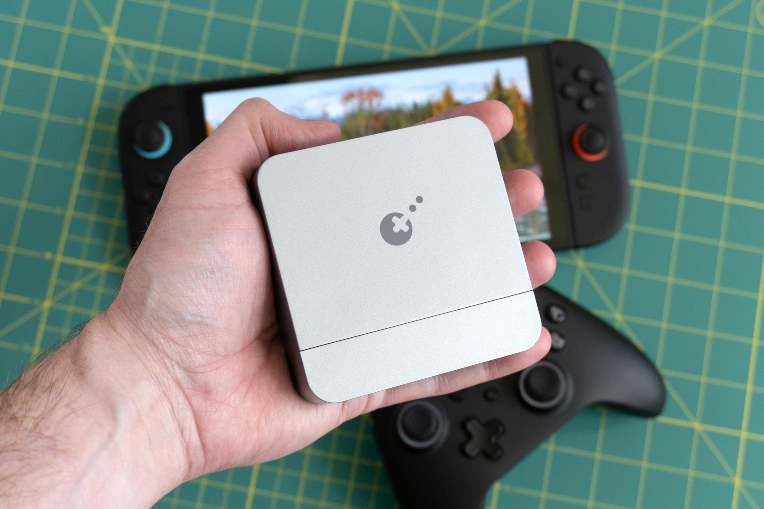 A person holds the GuliKit Dock for Switch 2 above a Nintendo Switch 2 console and a controller.