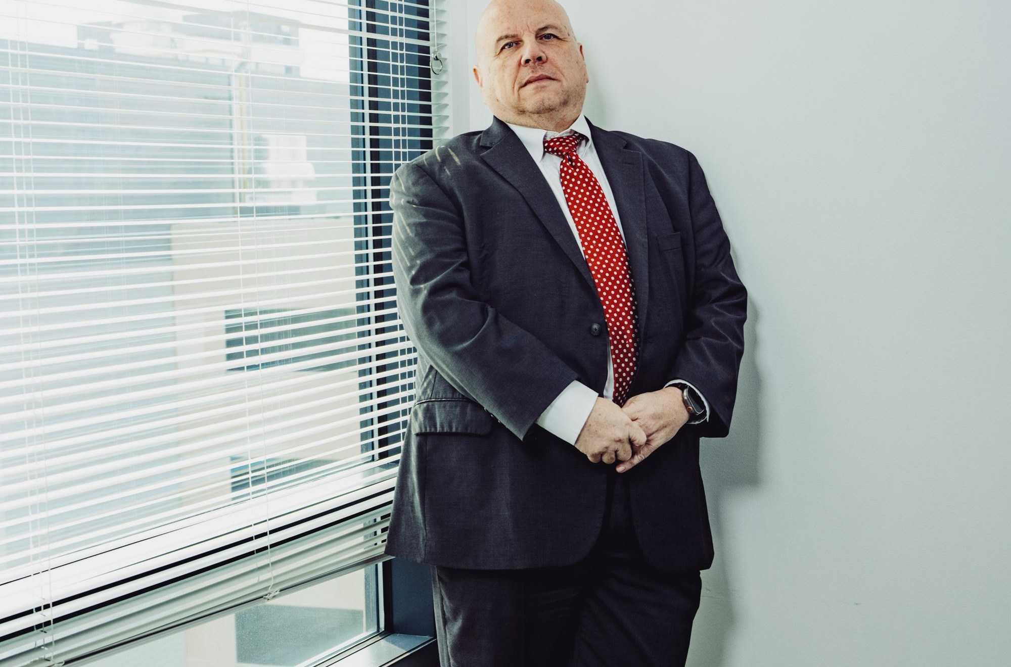 Buddy Rizer, an older man wearing a suit, poses for a portrait near the window in his office.