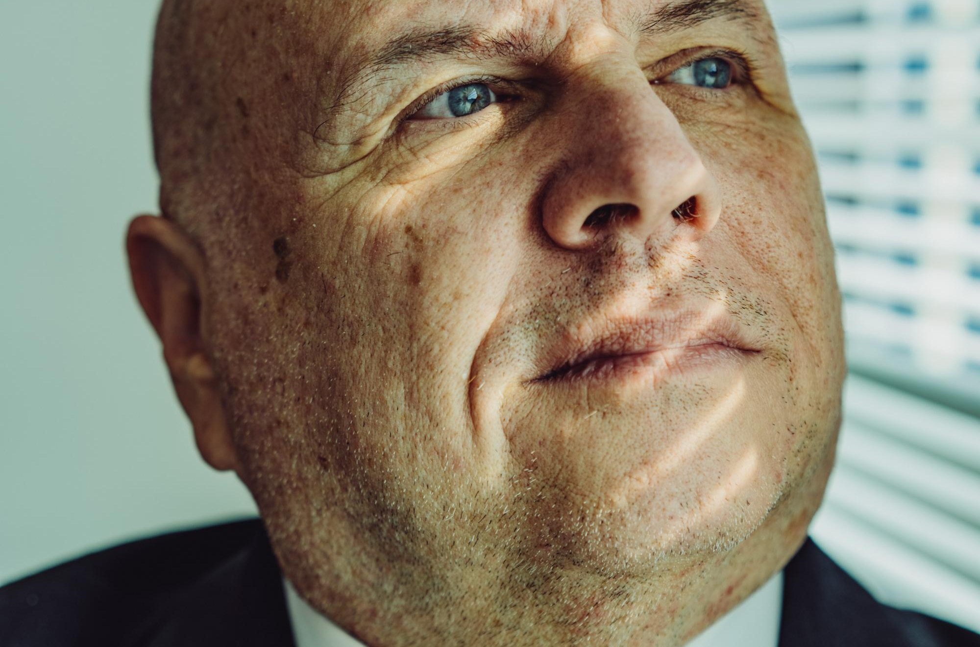 Buddy Rizer, an older man wearing a suit, poses for a portrait near the window in his office.