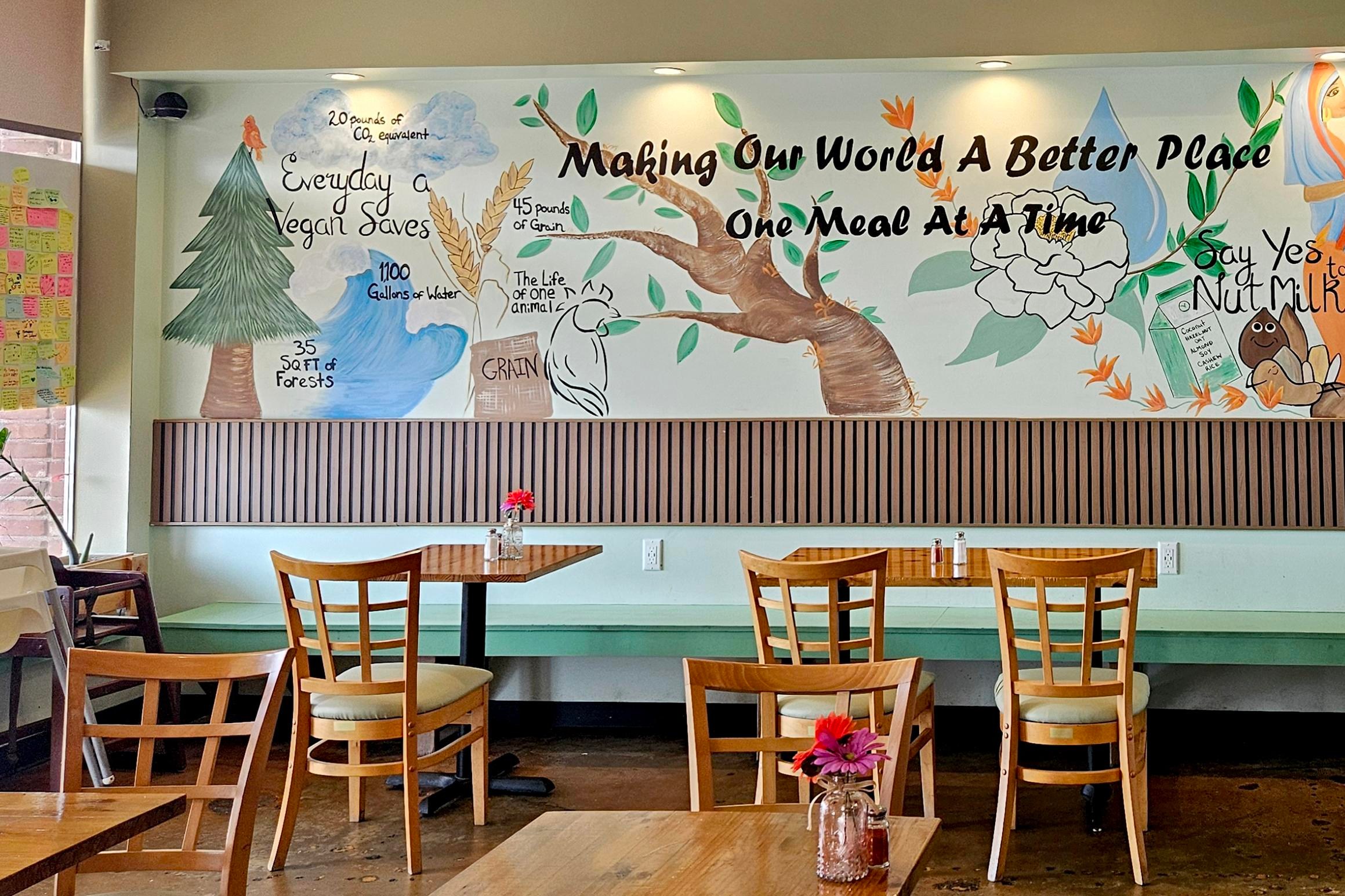 a painted mural on the wall of a cafe reads “Making our world a better place one meal at a time” and depicts various natural elements and food items.