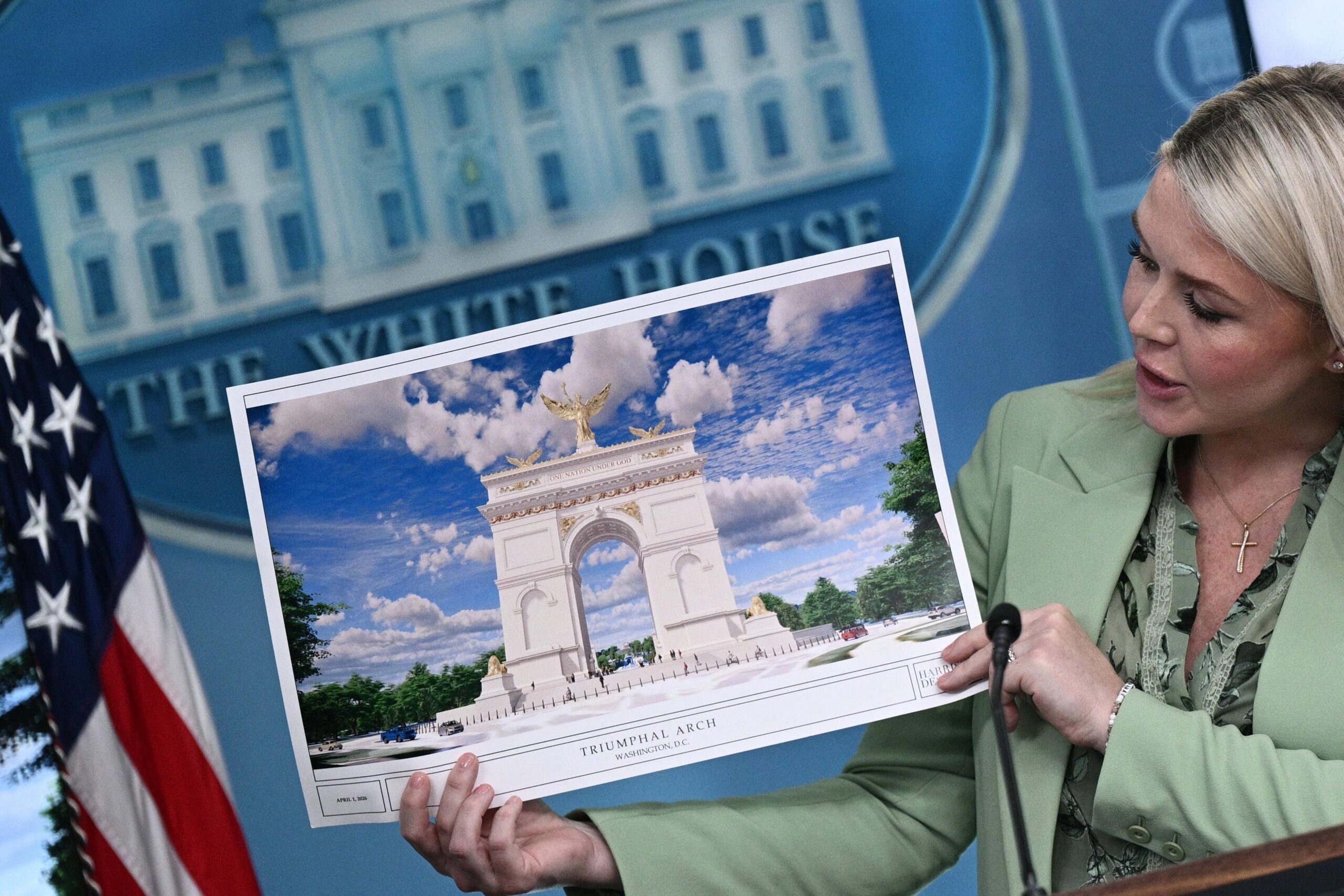 Karoline Leavitt, a blonde woman wearing a pale green blazer and blouse, holds a printout depicting Trump’s proposed triumphal arch.