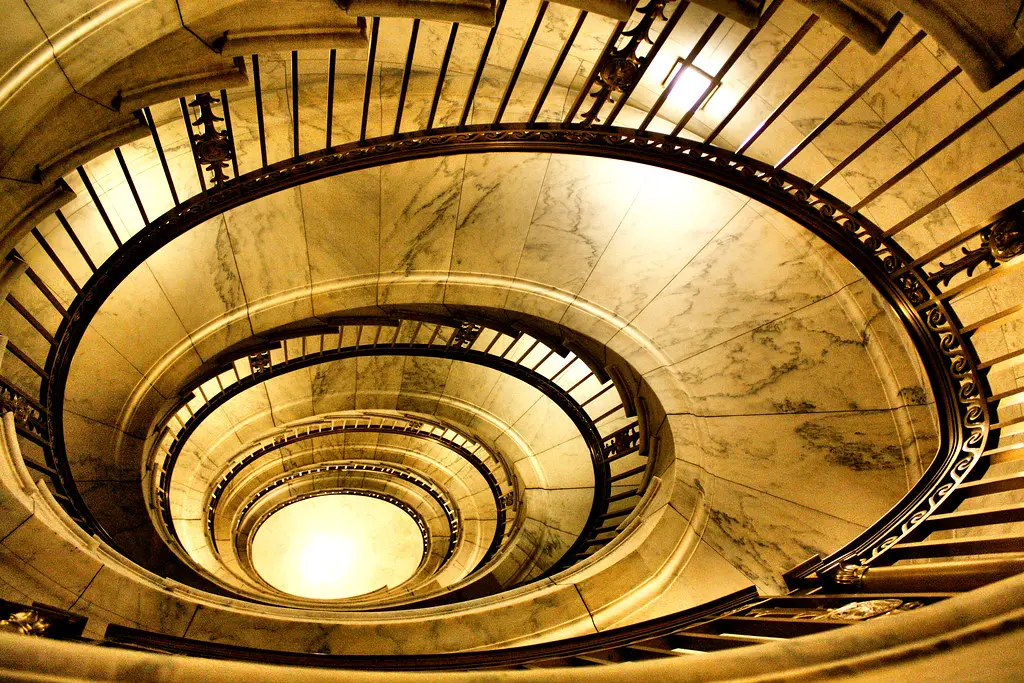 A low-angle shot looking down into a grand, spiral marble staircase with ornate railings.